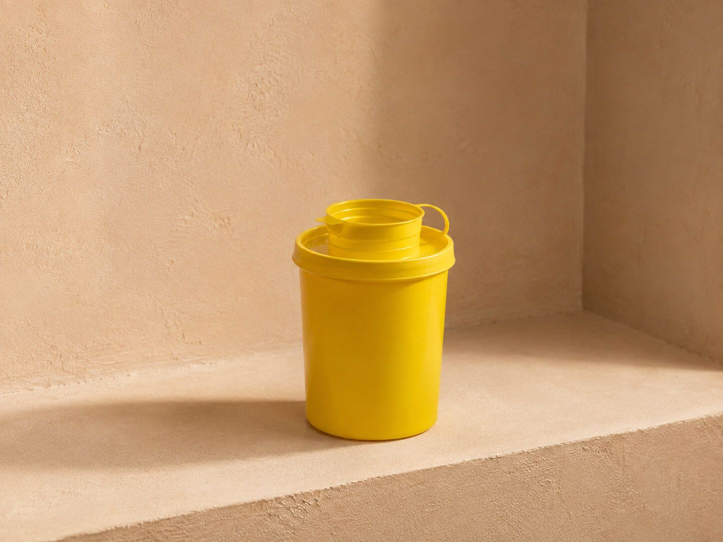 A vibrant yellow cylindrical container with a nested cup lid sits on a beige surface.