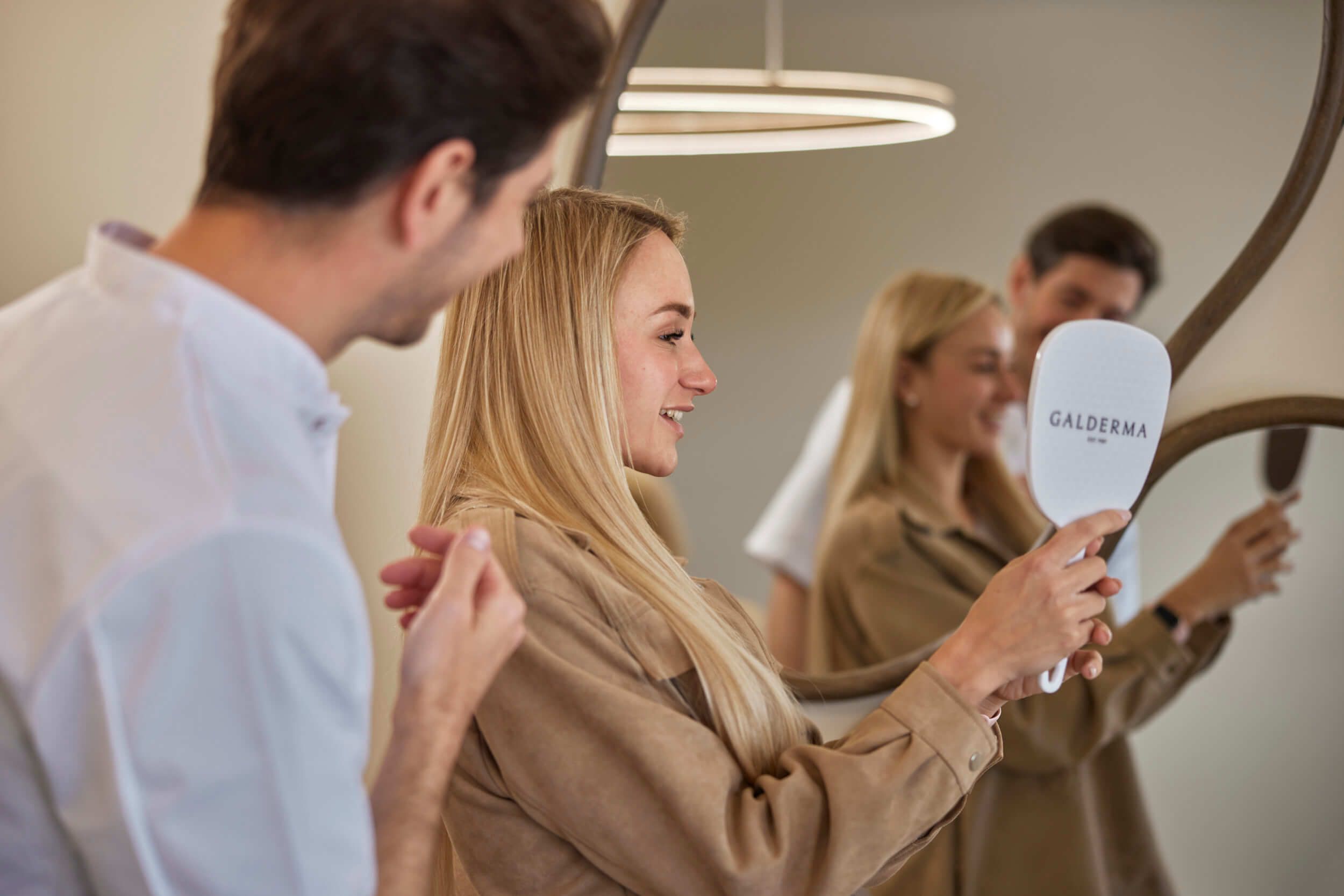 Wat maakt onze kliniek bijzonder: deskundige professionals en persoonlijke zorg bij The Body Clinic mirror while aesthetician stands beside her in a clinic.