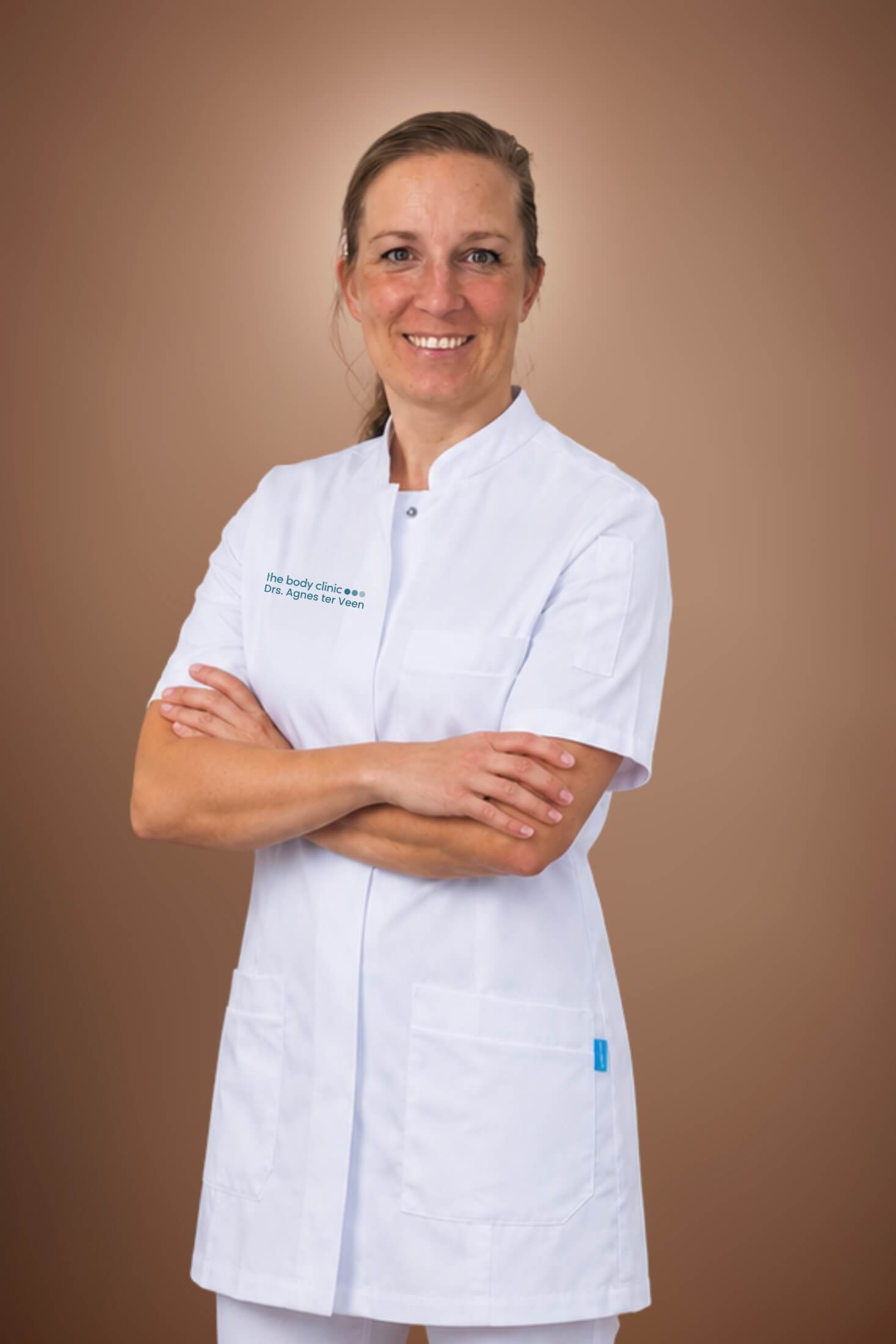 Smiling woman in white medical uniform and glasses with arms crossed.