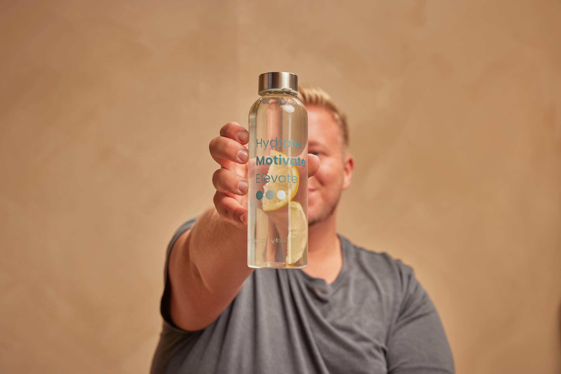 A person holds out a clear glass water bottle containing water and lime slices.