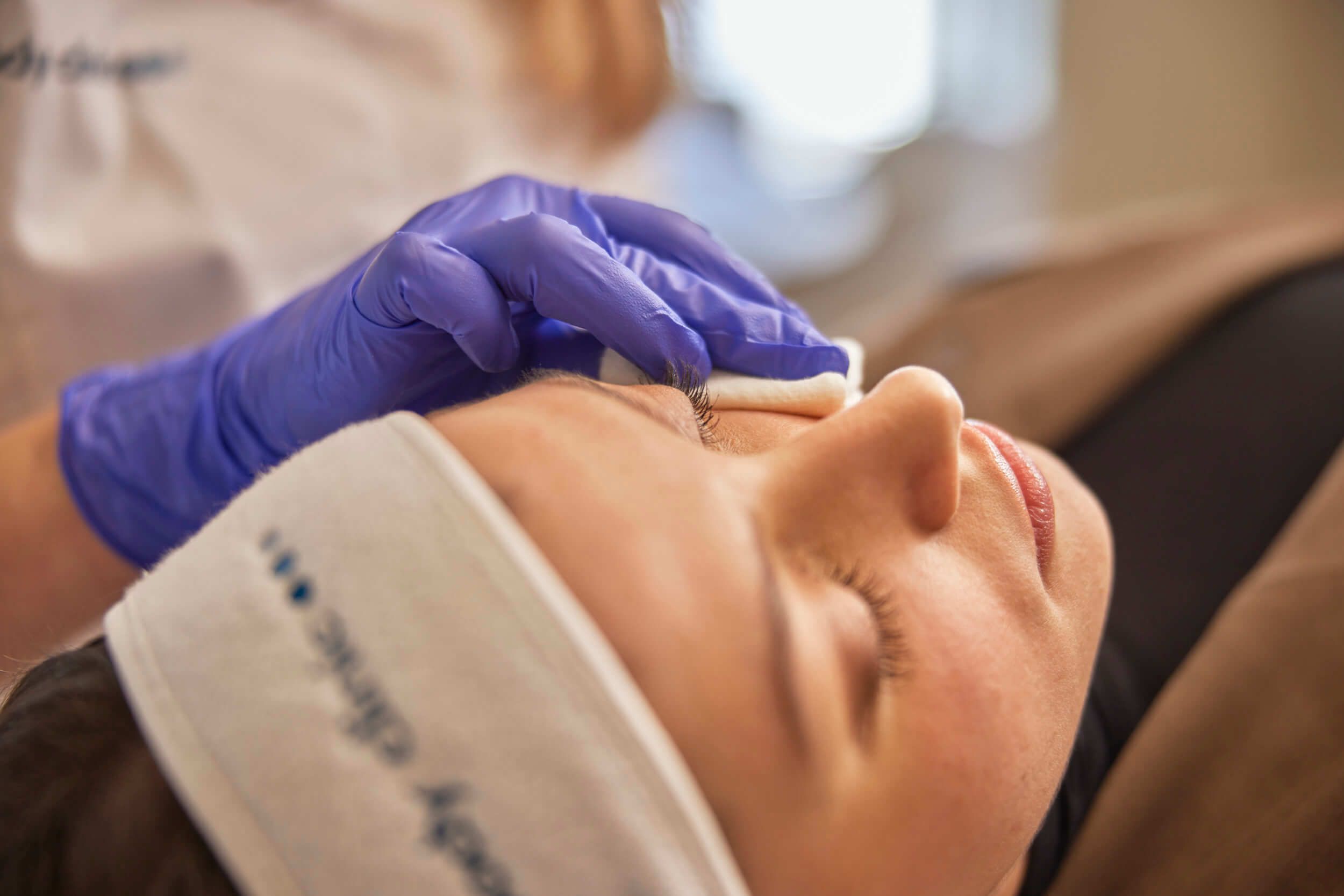 Huidtherapeut reinigt gezicht van client ter voorbereiding op een huidtherapie behandeling bij The Body Clinic