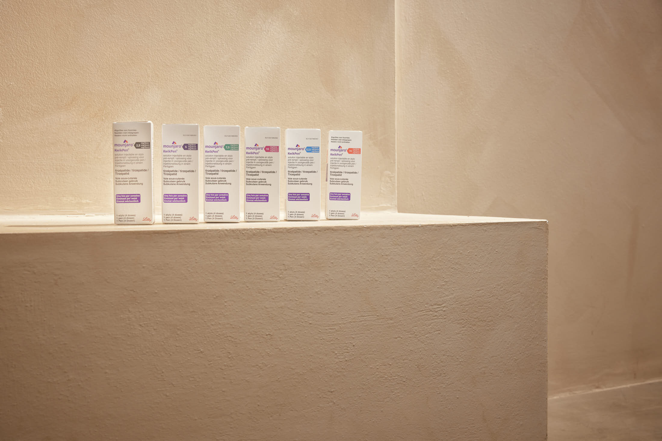 Seven clear bottles with colorful labels and purple liquid stand on a light brown shelf.
