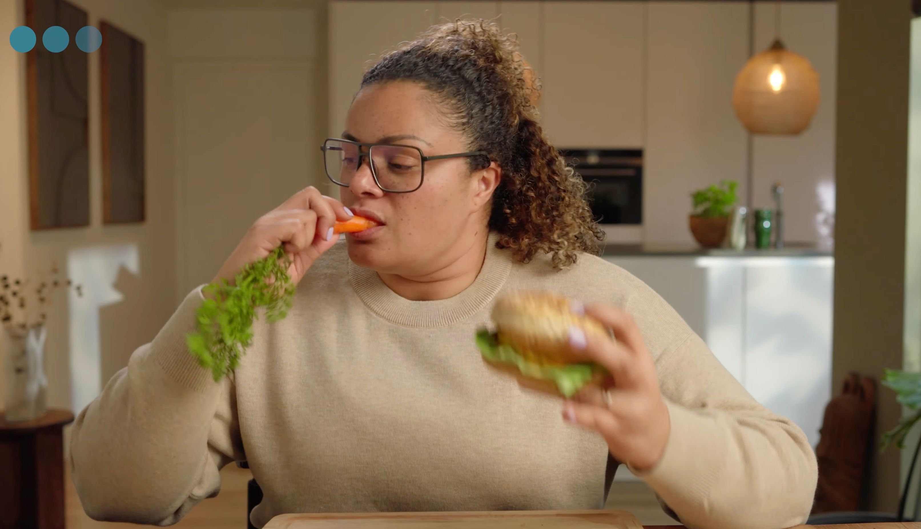 Woman eating a raw carrot while holding a burger, indicating contrasting food choices.