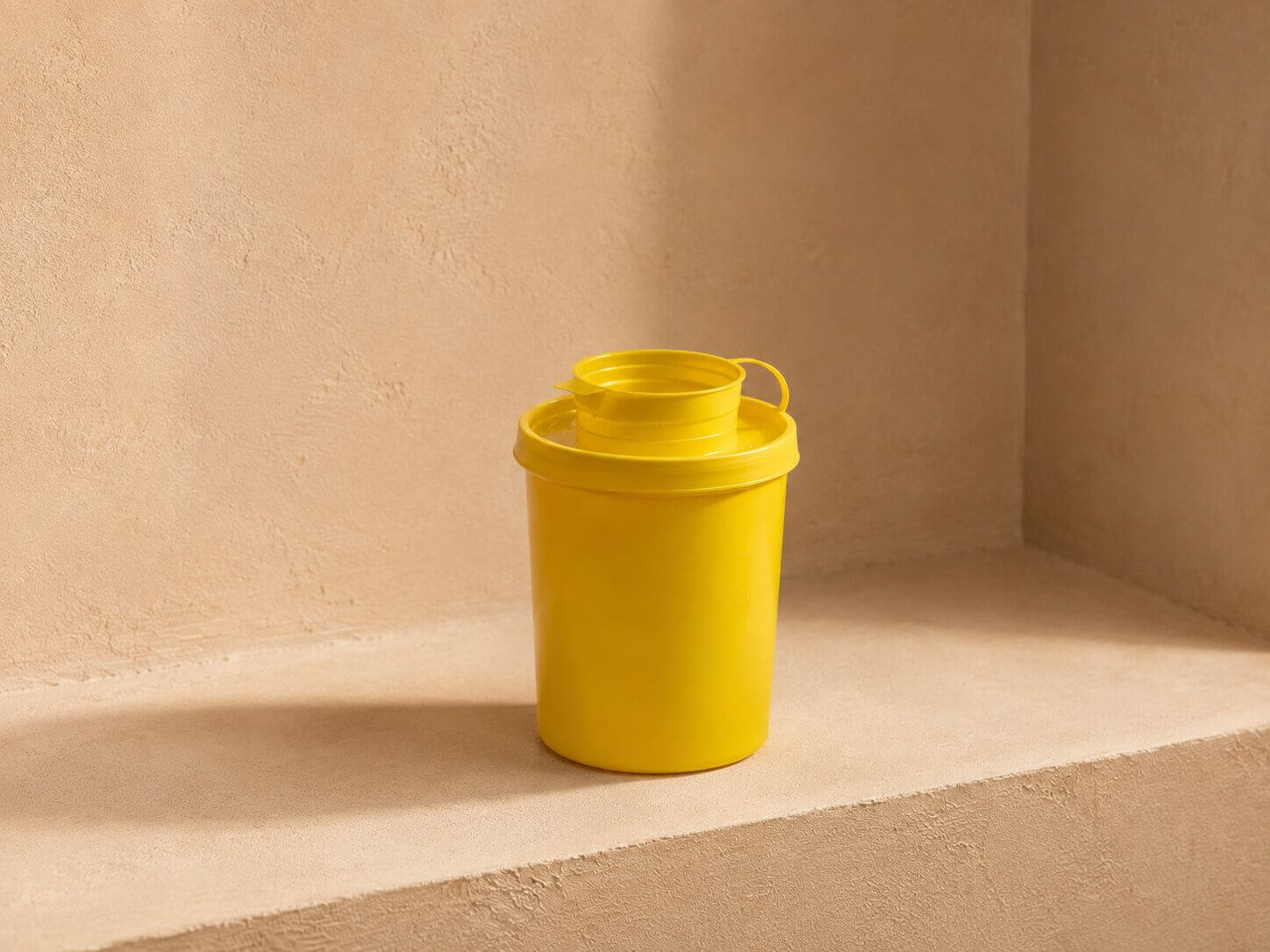 Bright yellow cylindrical container with a matching lid on a minimalist beige shelf.