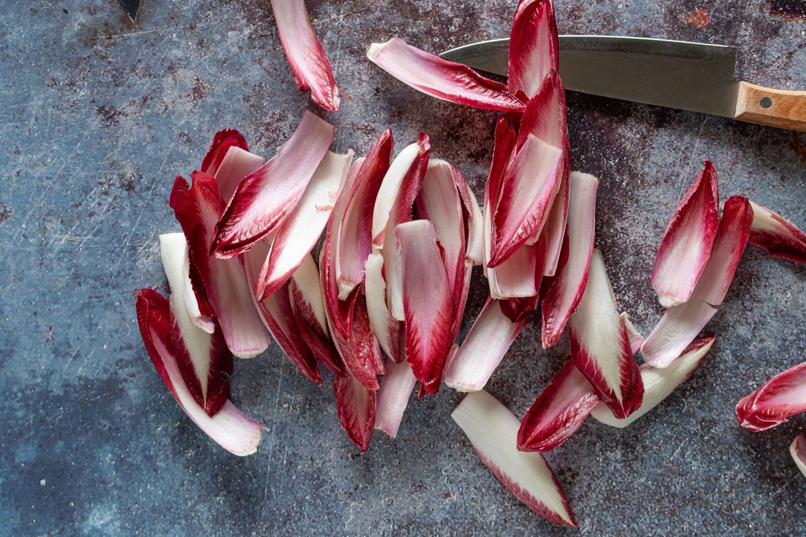 Red and white radicchio leaves, some chopped, with a knife on a grey surface.