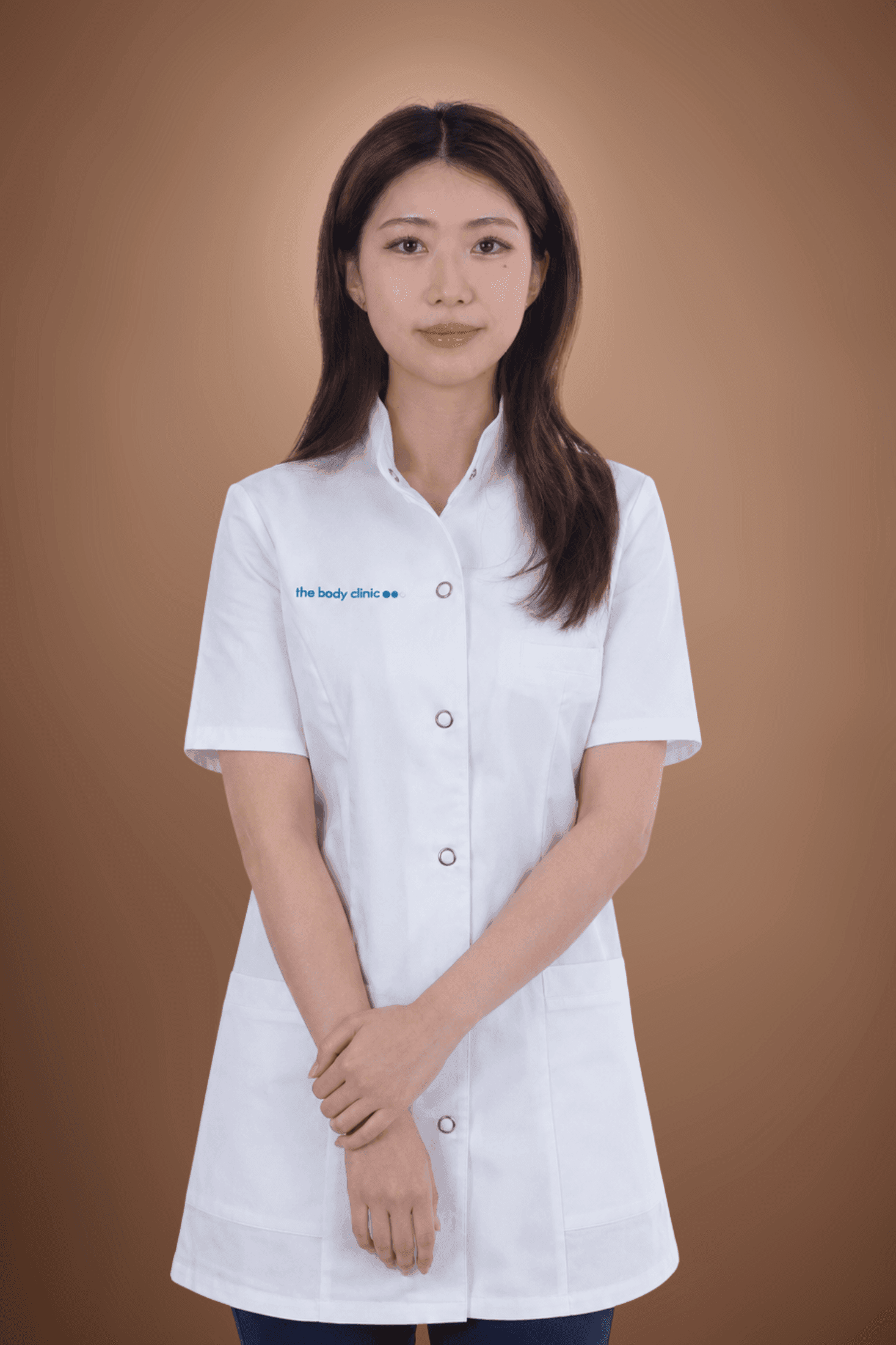 Young Asian woman in white medical uniform with crossed arms and confident expression.