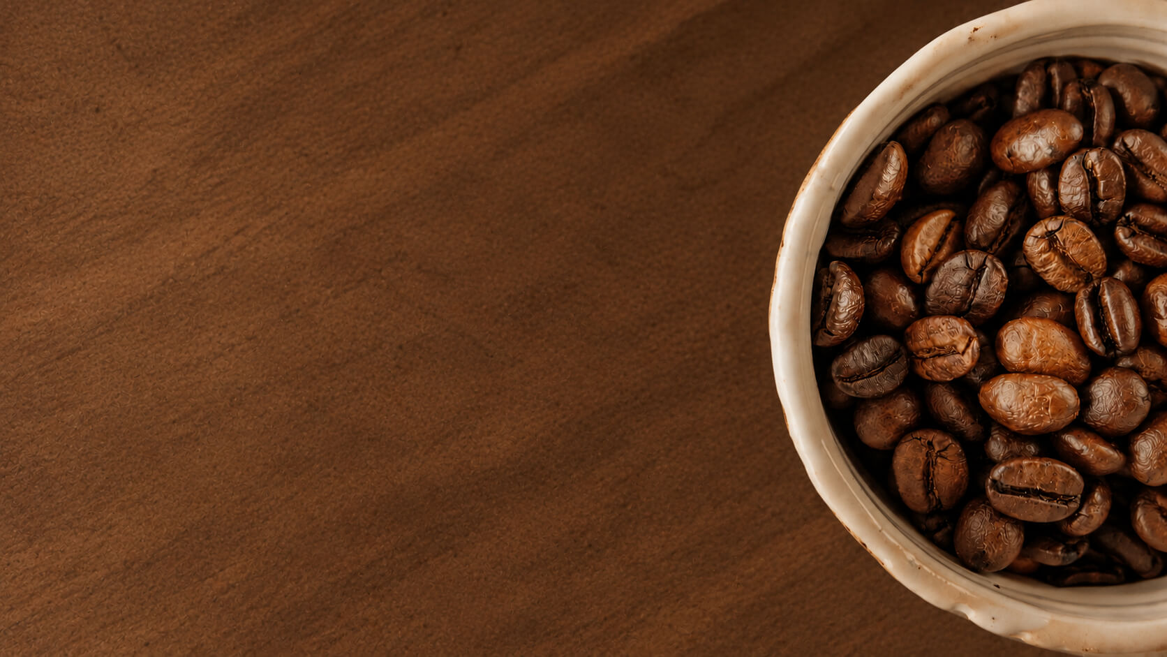 Geroosterde koffiebonen in een lichte bak op een donkere houten ondergrond, als illustratie bij koffie en afvallen.