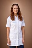 Smiling woman with long brown hair wearing a white medical lab coat.