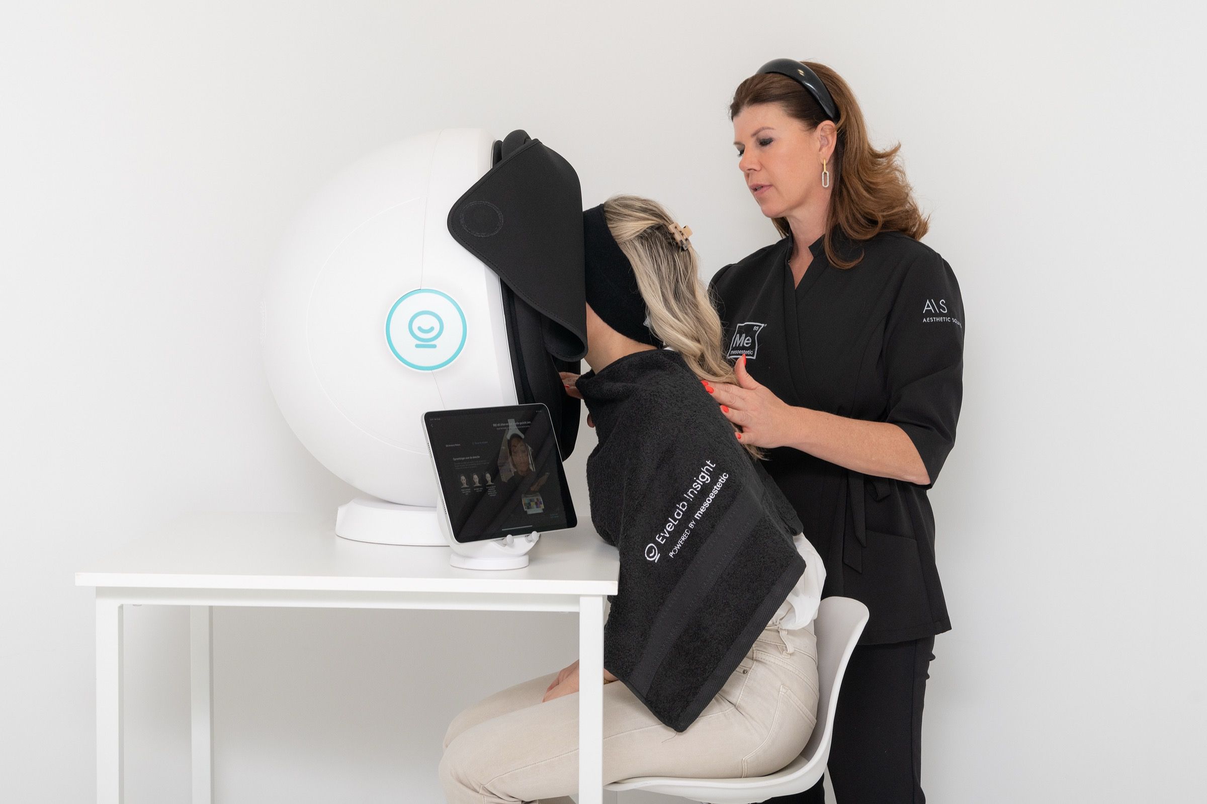 Woman with face and shoulders covered by a black drape in a skin analysis machine.
