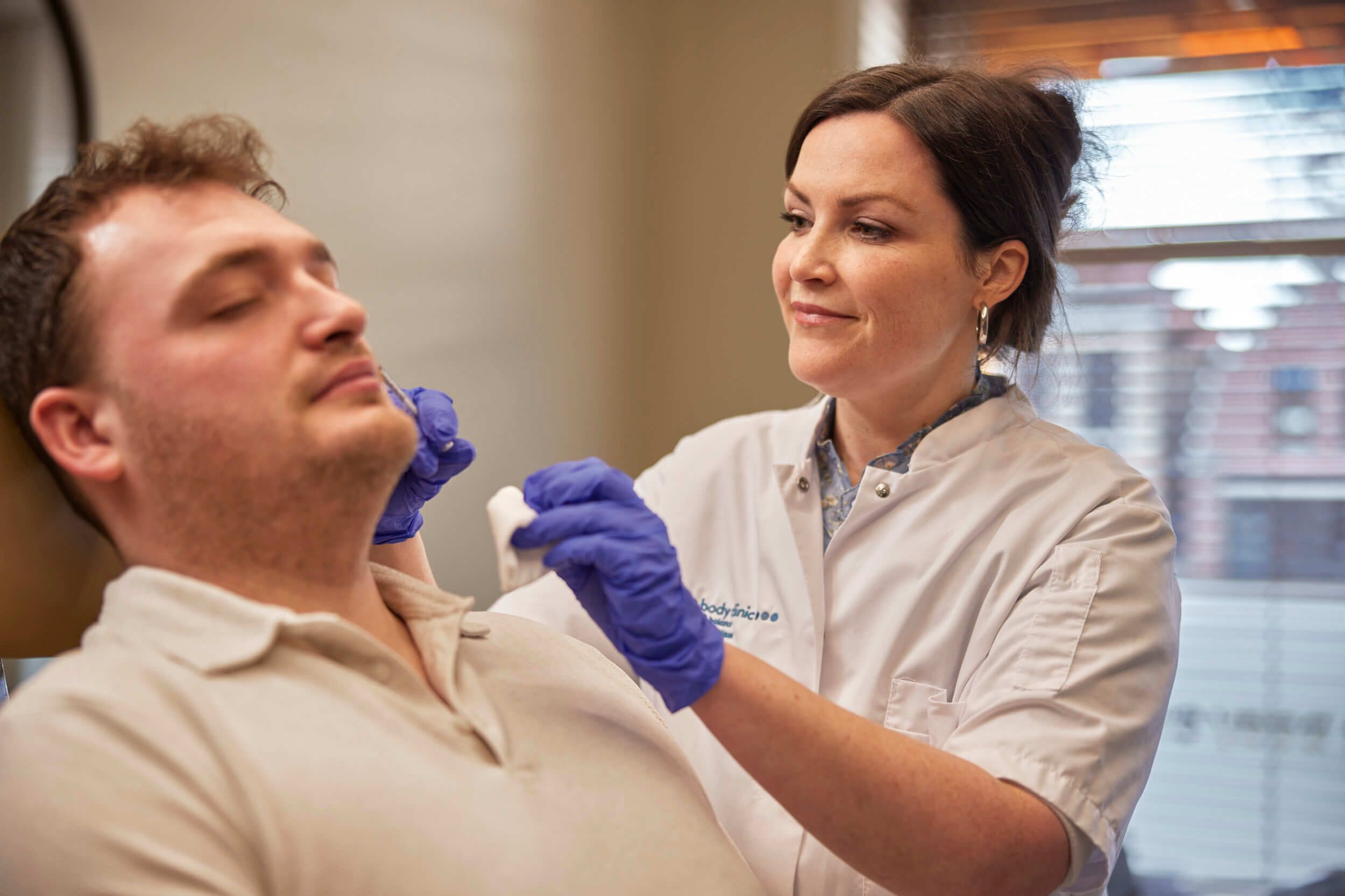 Medical professional in blue gloves treats a man's jaw area with a white pad.