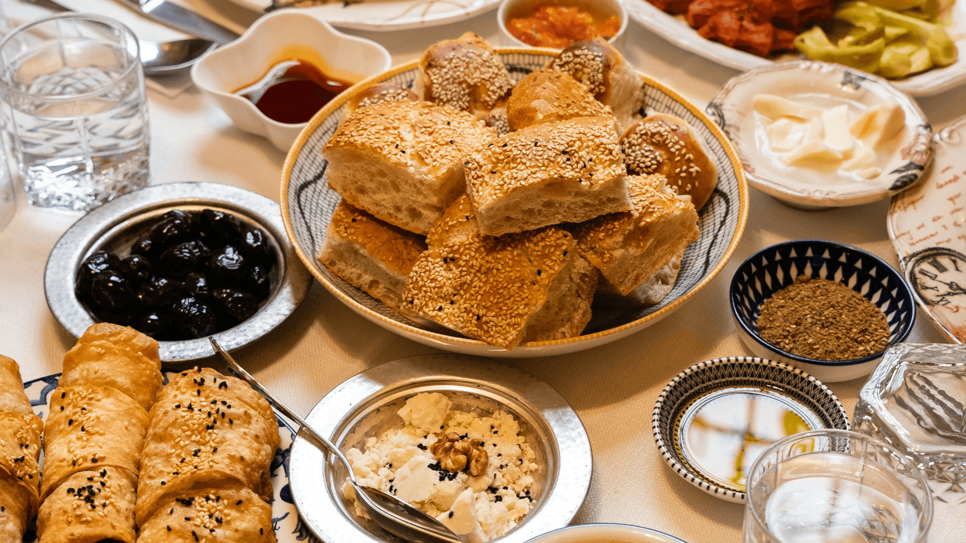 A lavish breakfast table with bread, olives, pastries, butter, and cheese spread.