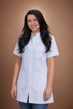 Smiling young woman with dark hair wearing a white medical coat and blue jeans.