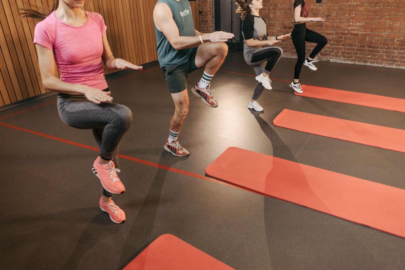 Four people doing high-knee exercises on red mats in a fitness studio.