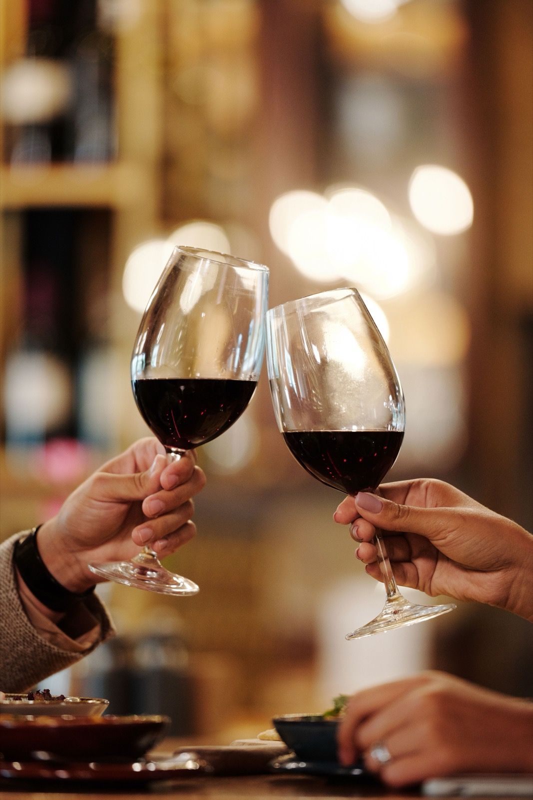 Two hands clinking wine glasses filled with red wine in a celebratory toast.