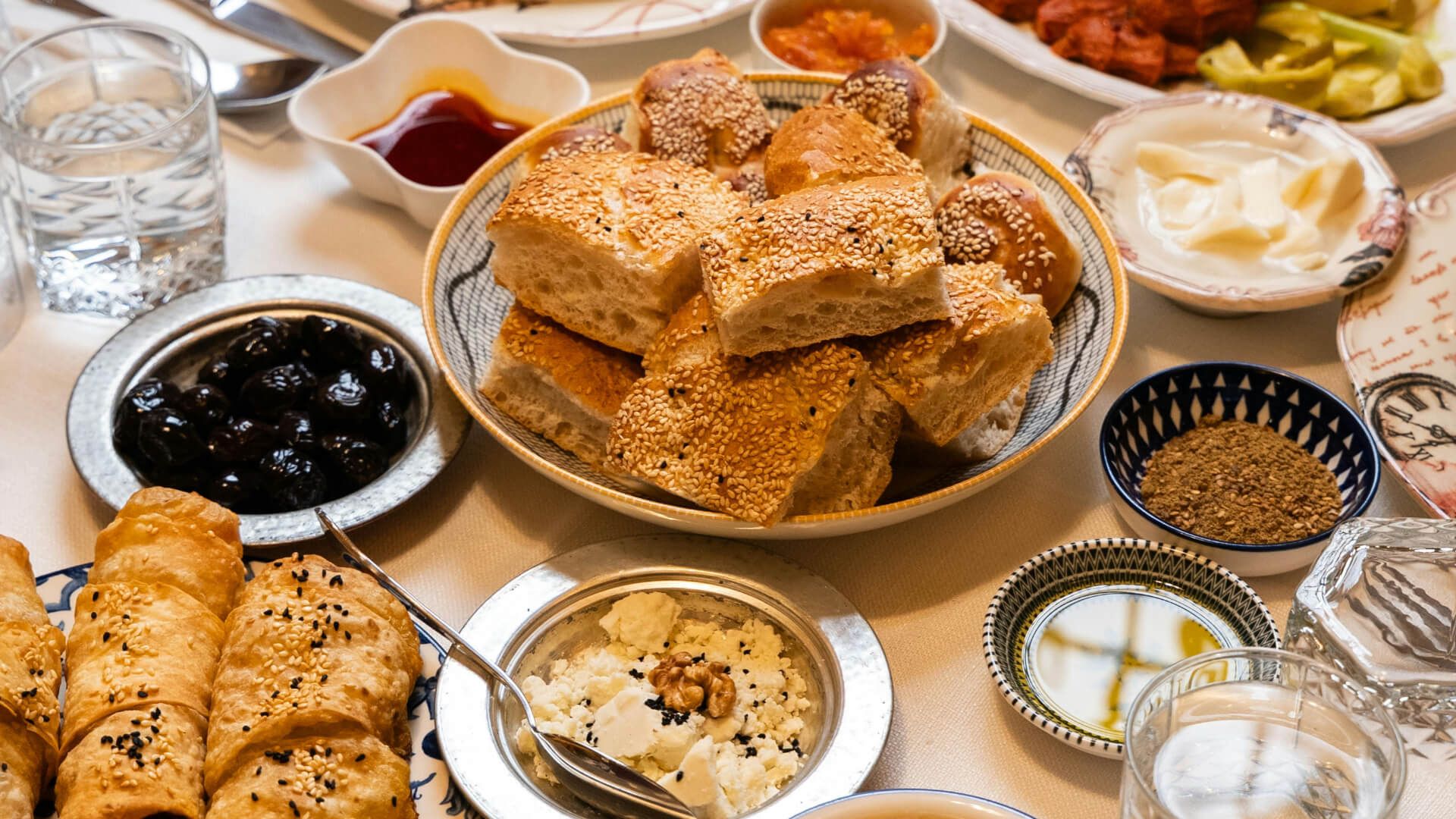 A table spread with a variety of Mediterranean breakfast foods: bread, pastries, dips.