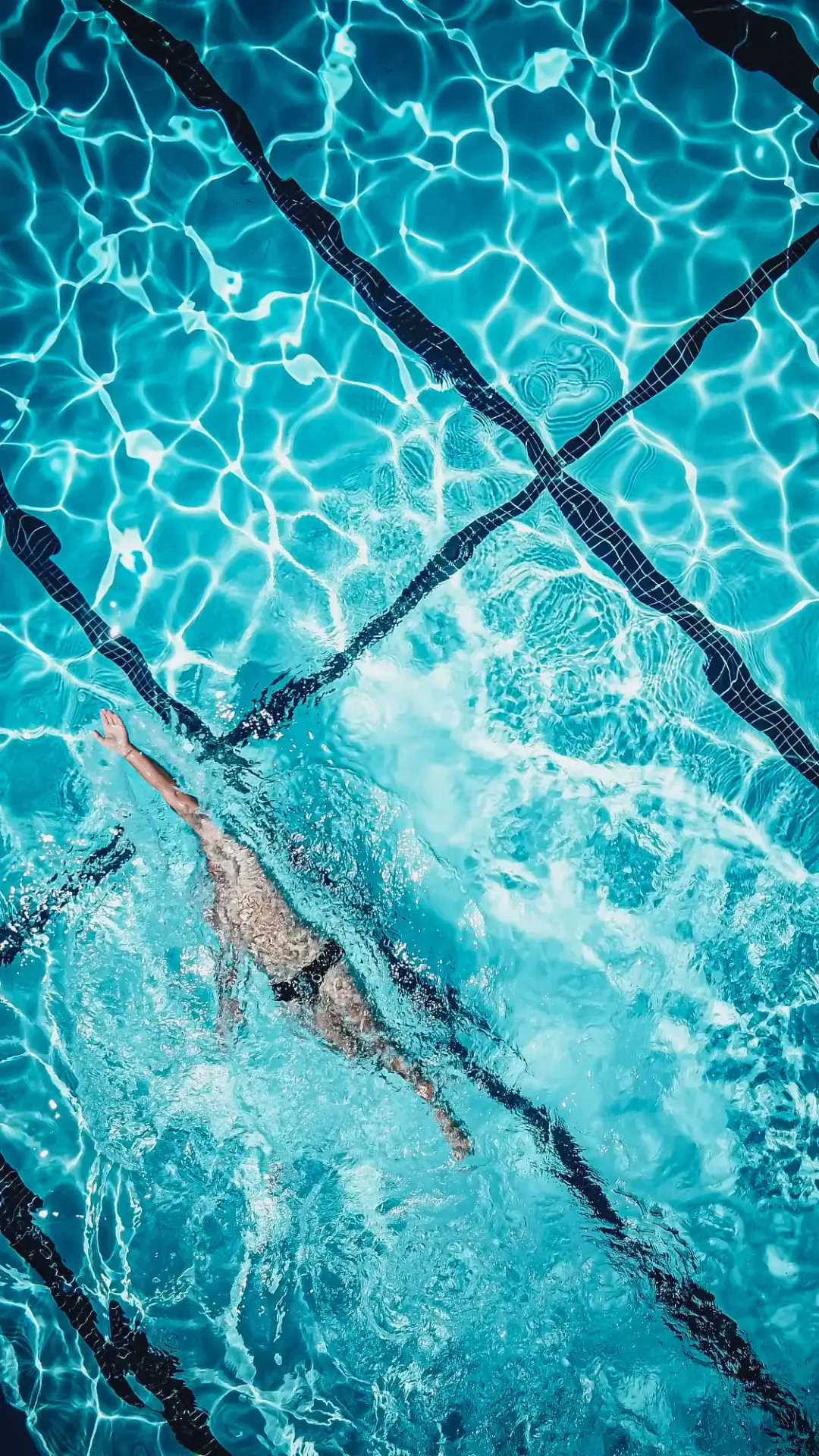 Person swimming freestyle underwater in a bright blue pool with visible lane lines.