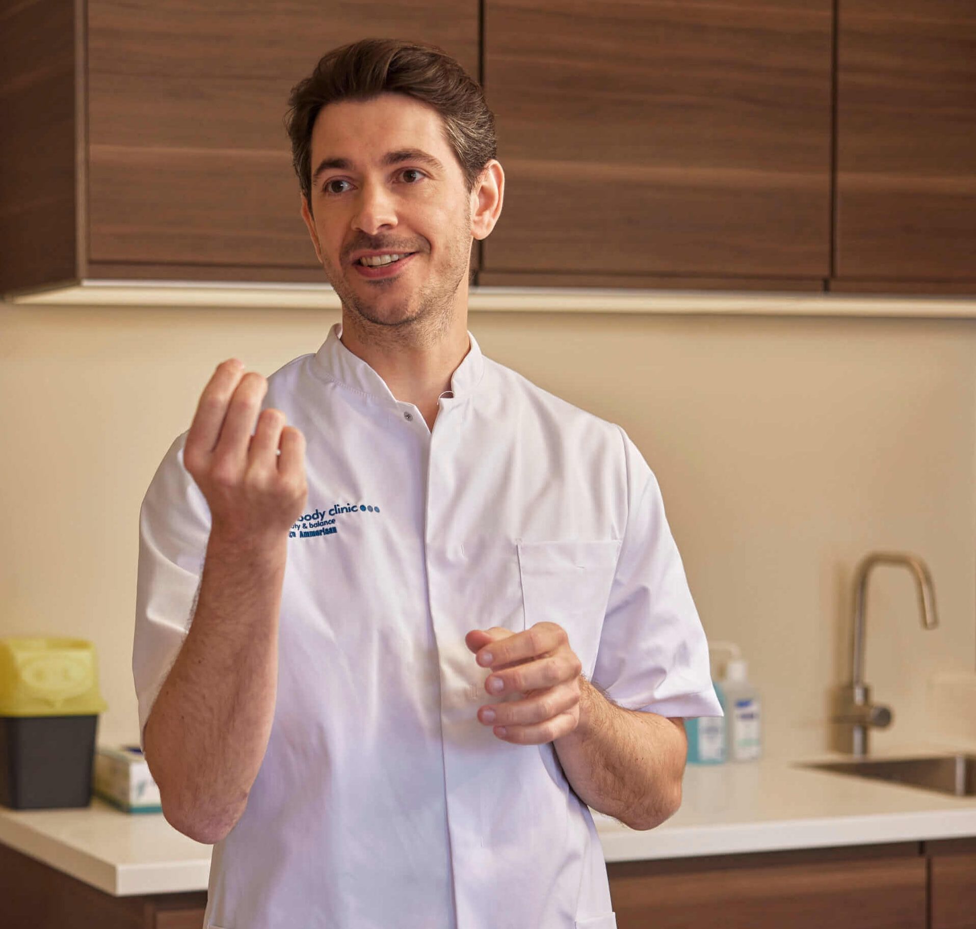 Man in a white medical coat gesturing with his hands, explaining something small.