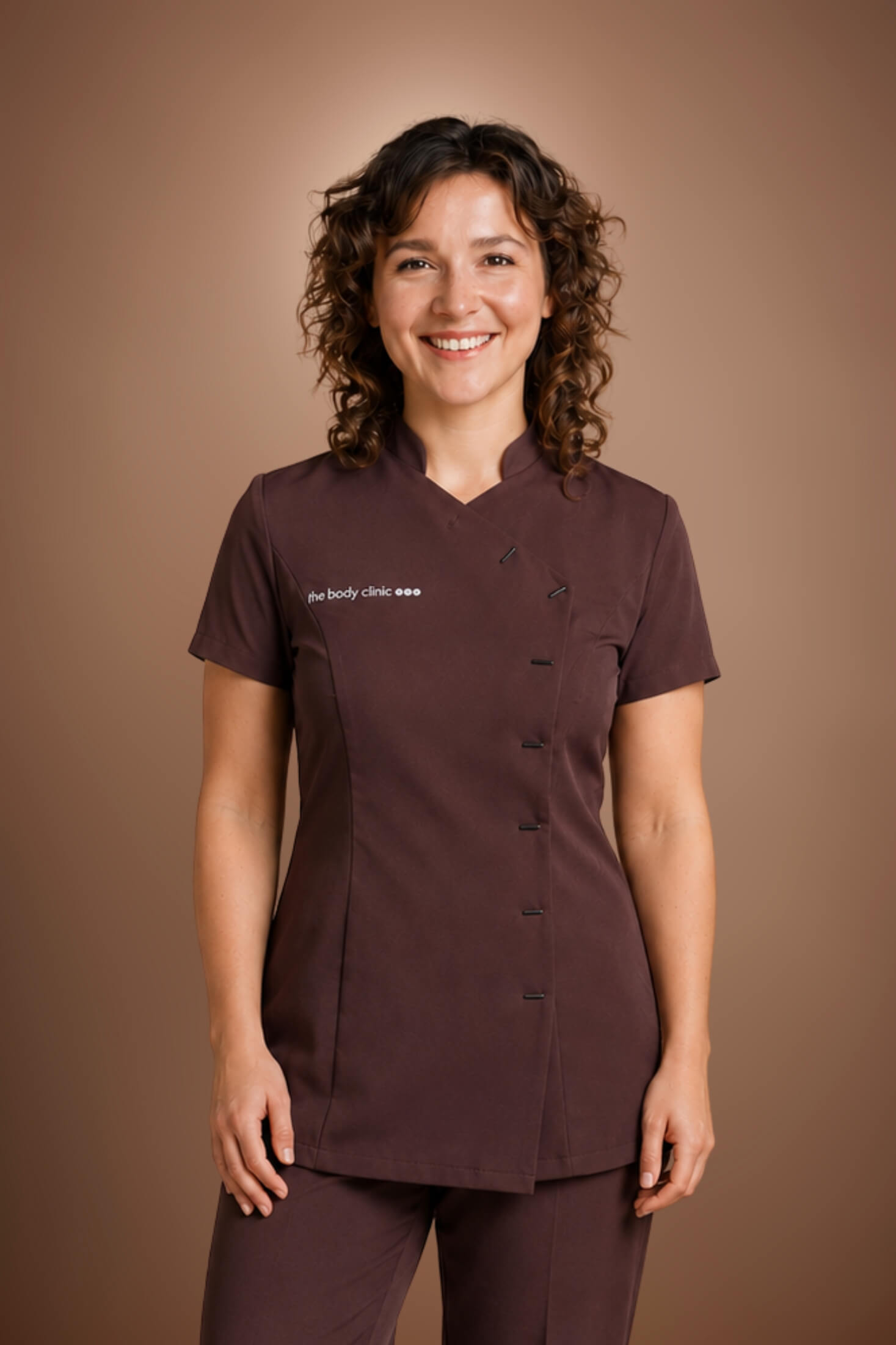 Smiling woman in a brown CACI SYNERGY uniform standing against a brown background.