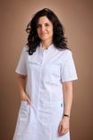 Smiling woman with dark hair in a white lab coat standing confidently.
