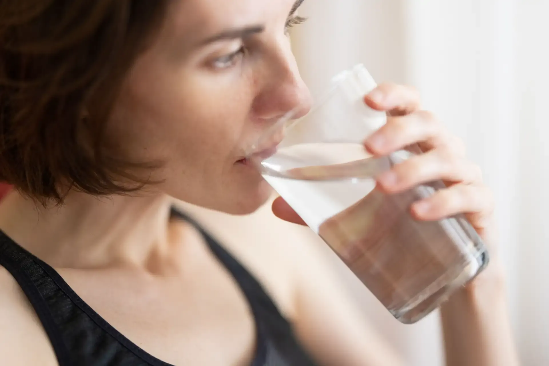 Woman drinking water from a clear glass, emphasizing the importance of hydration.