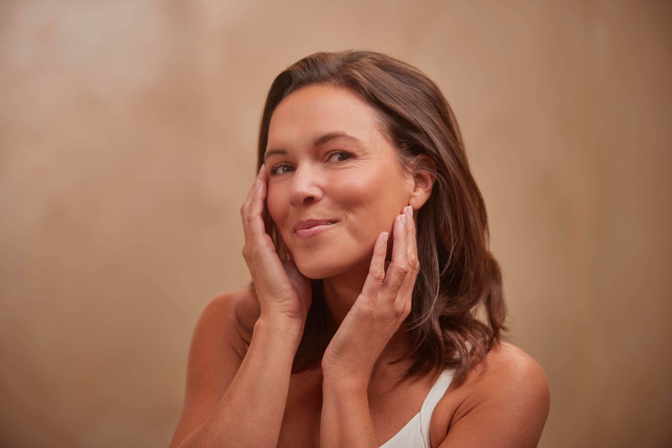 Vrouw raakt haar gezicht aan en toont een stralende, uitgeruste huid na carboxytherapie behandeling tegen donkere kringen bij The Body Clinic.