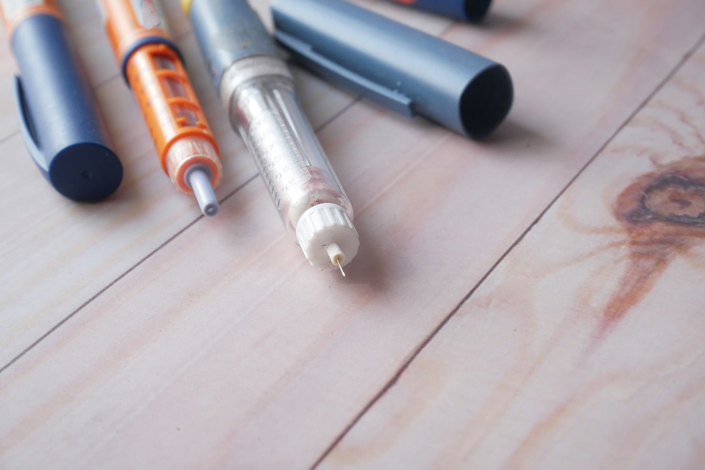 Multiple insulin pens with caps and needles visible on a light wooden table.
