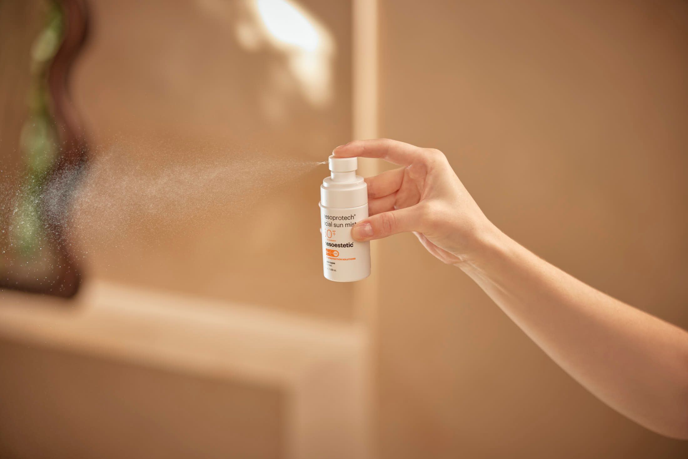 Hand holding white spray bottle emitting a fine mist into the air.