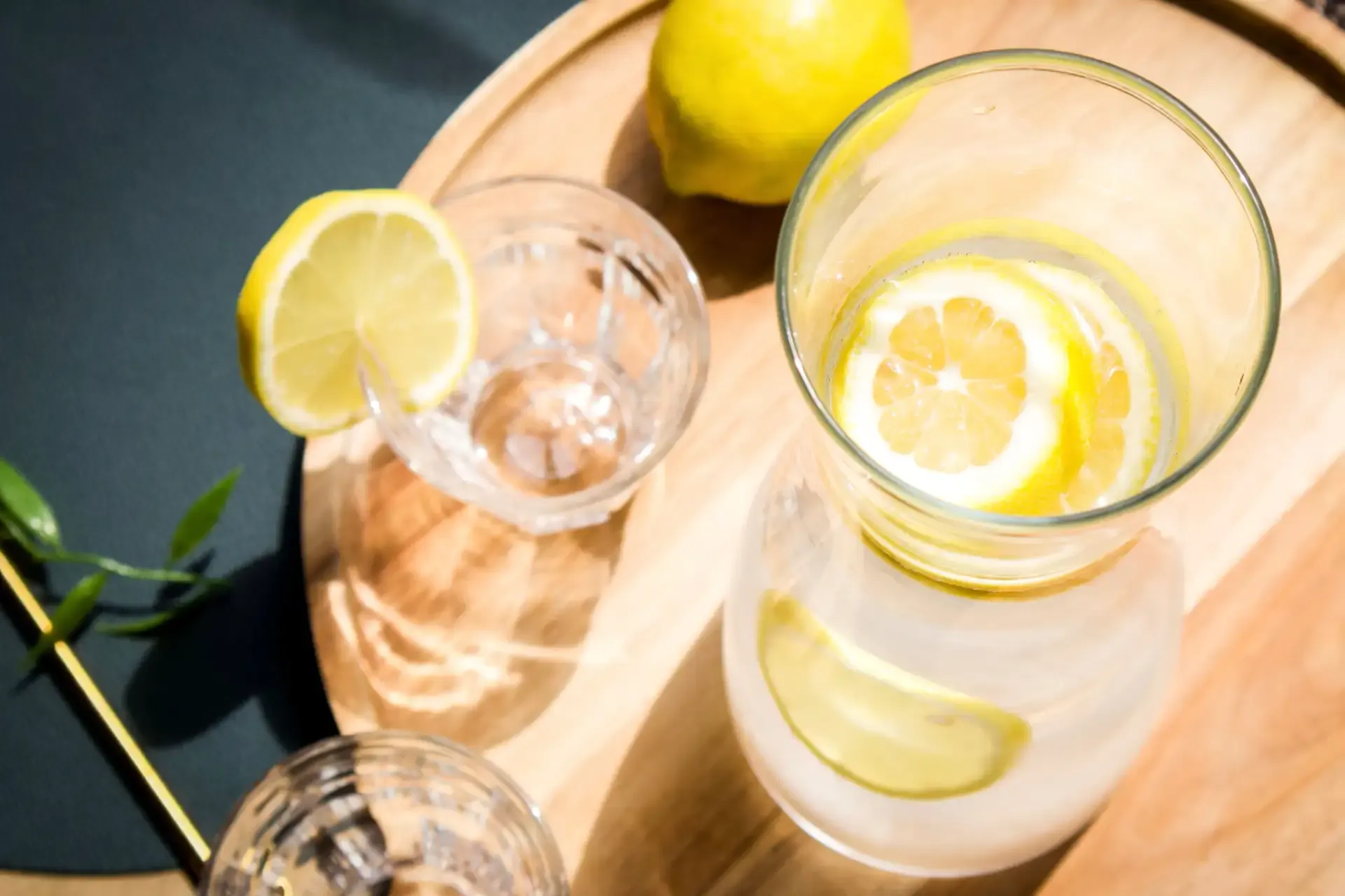 Refreshing lemon water in a pitcher and glasses on a wooden tray.
