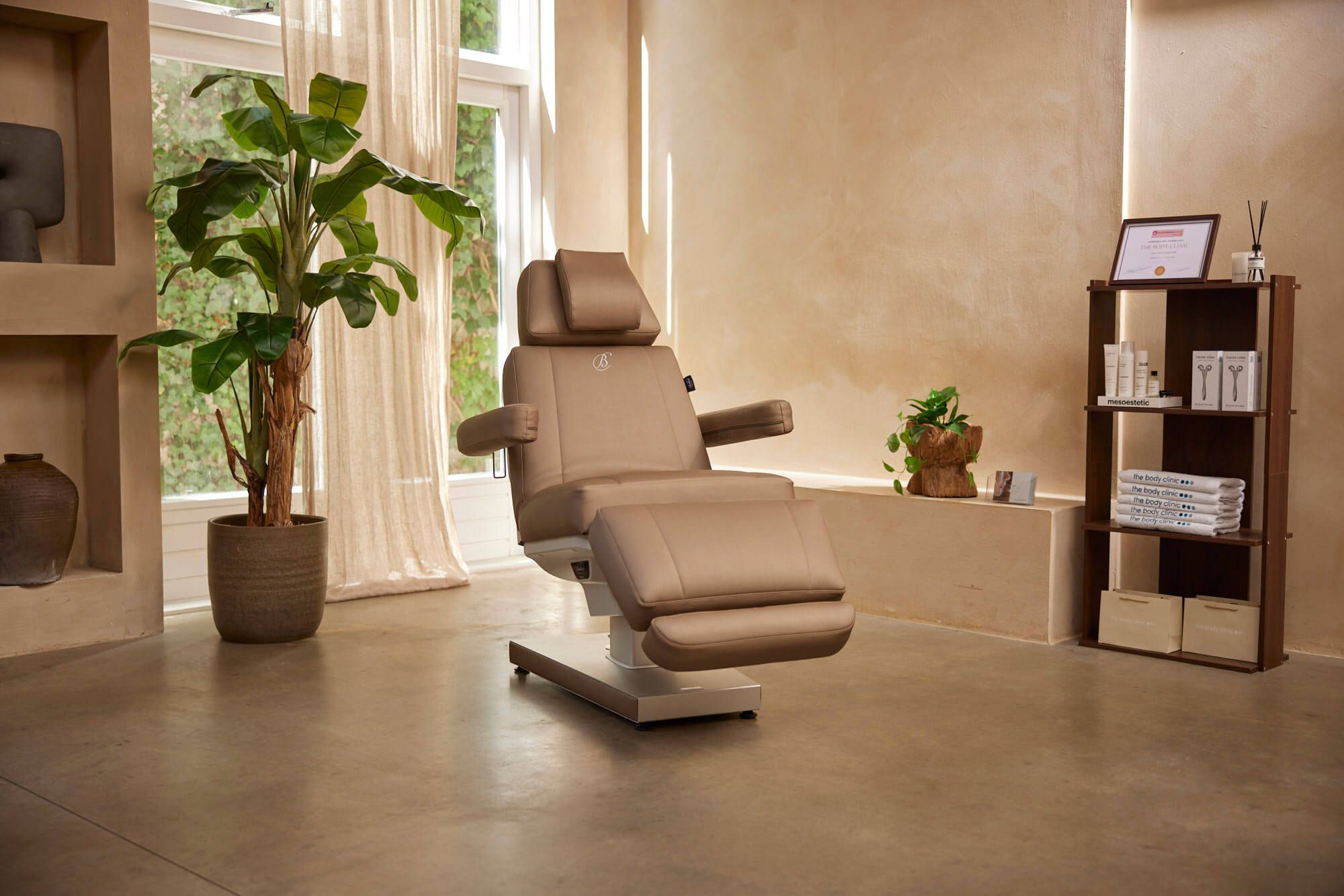 Luxe behandelkamer van The Body Clinic met een beige behandelstoel, planten en branded handdoeken