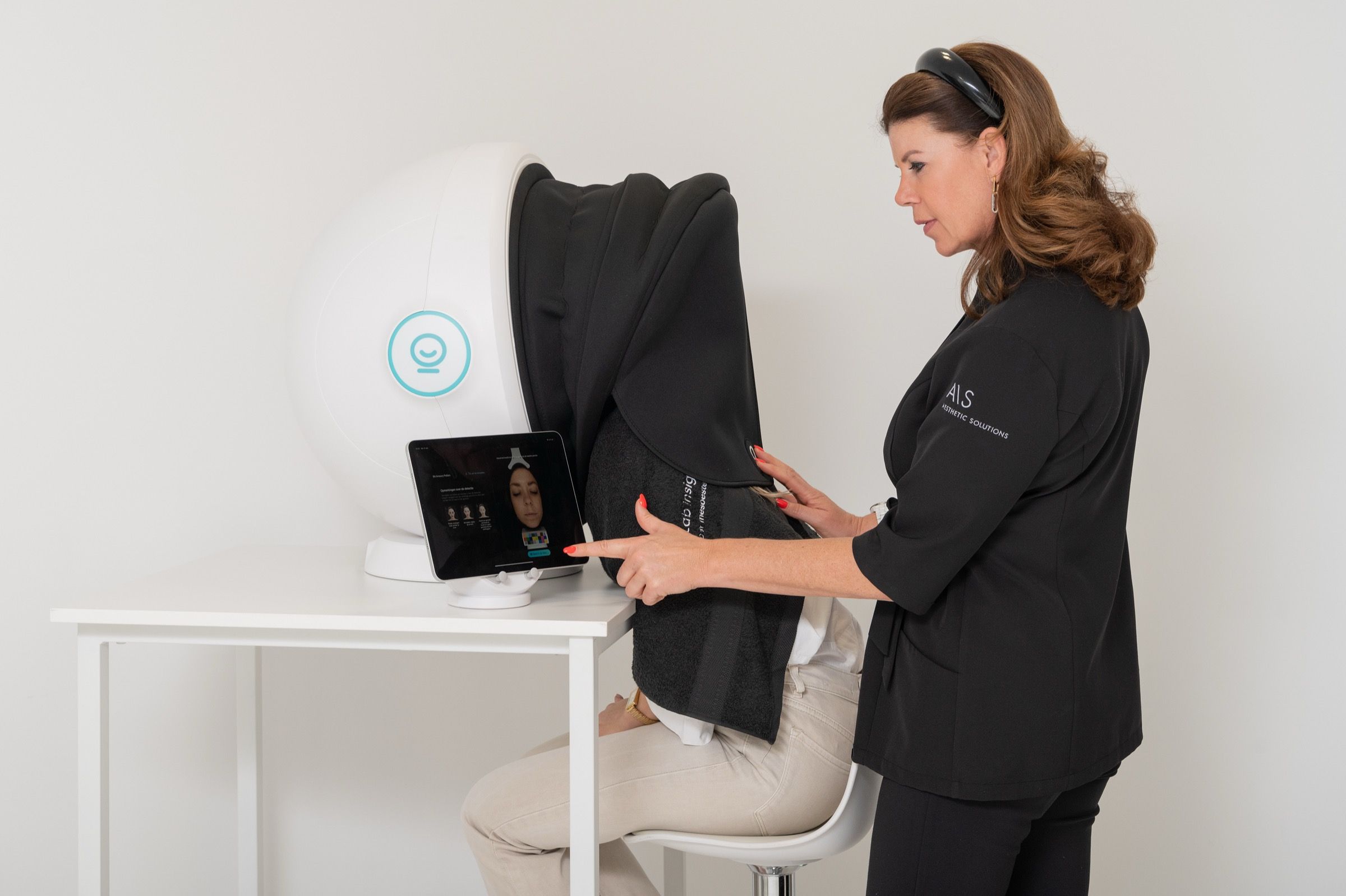 Technician points to tablet with skin analysis results next to client in machine.