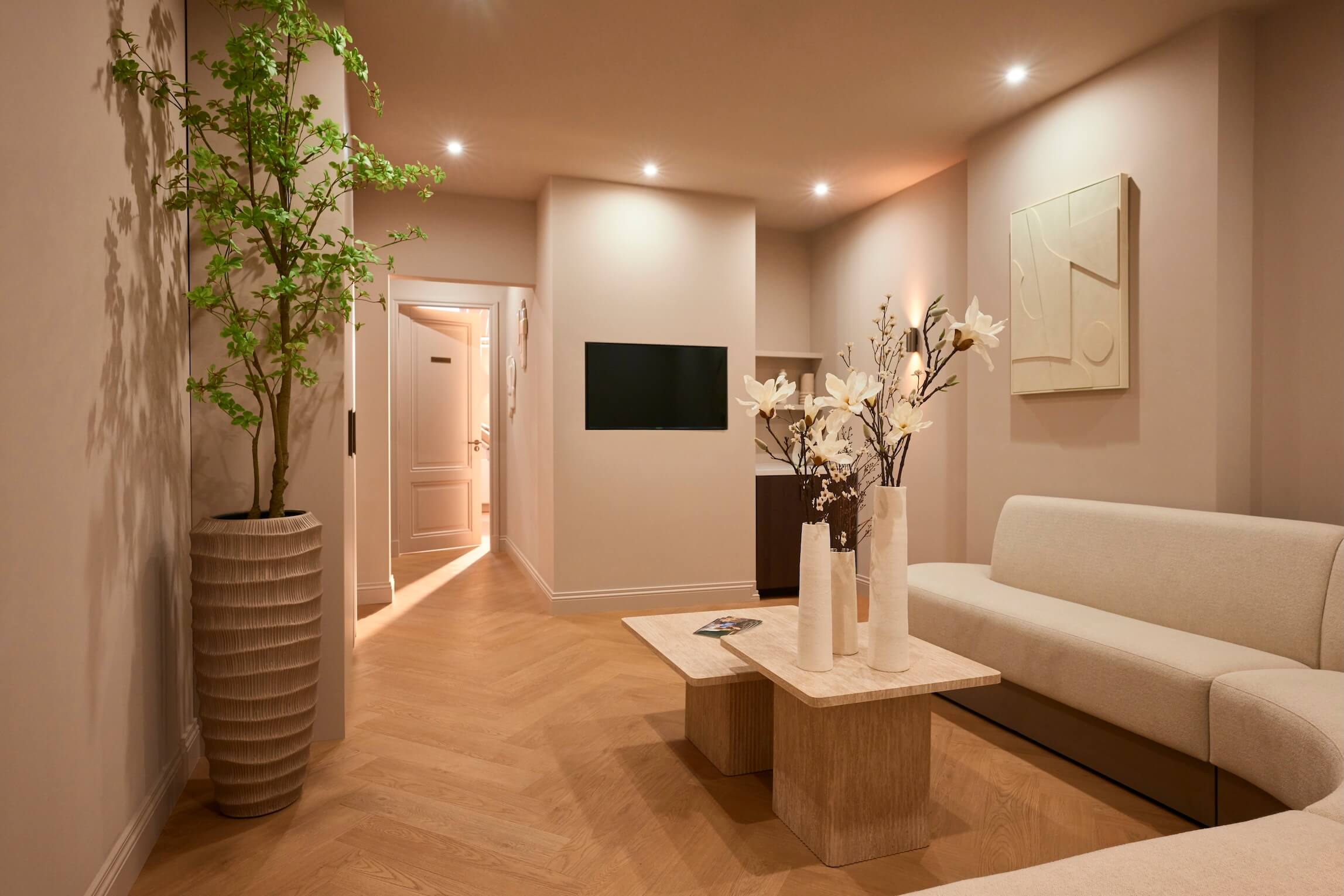 A modern, minimalist waiting room featuring a light sofa, coffee table, and potted plant.