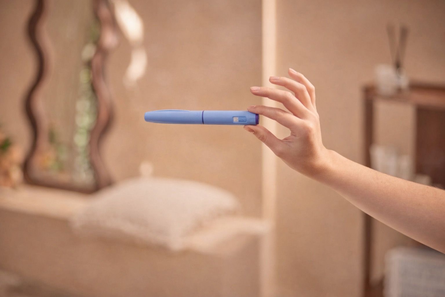 A person's hand holds a sleek, blue-purple, pen-like device in a soft bathroom background.