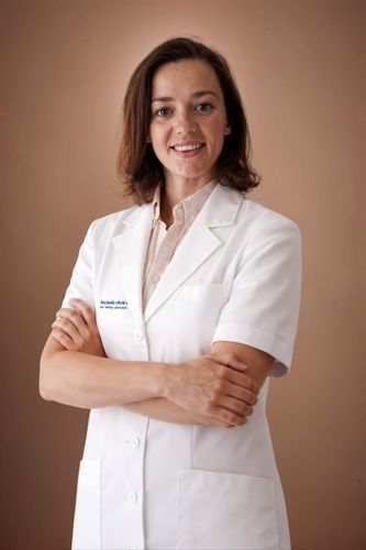 A smiling female medical professional in a white lab coat with crossed arms.