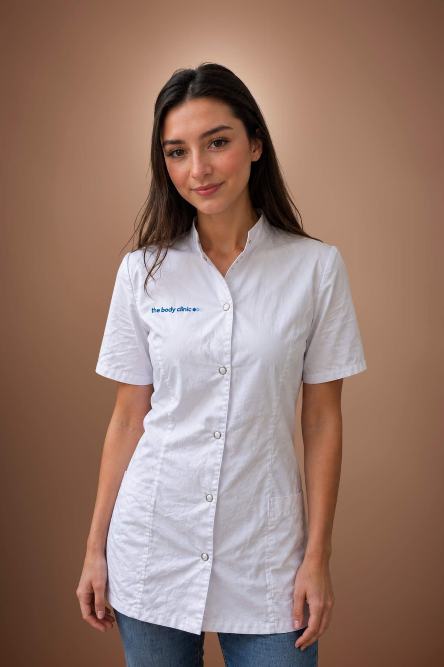 Young woman in a white medical scrub top smiles confidently, representing healthcare.