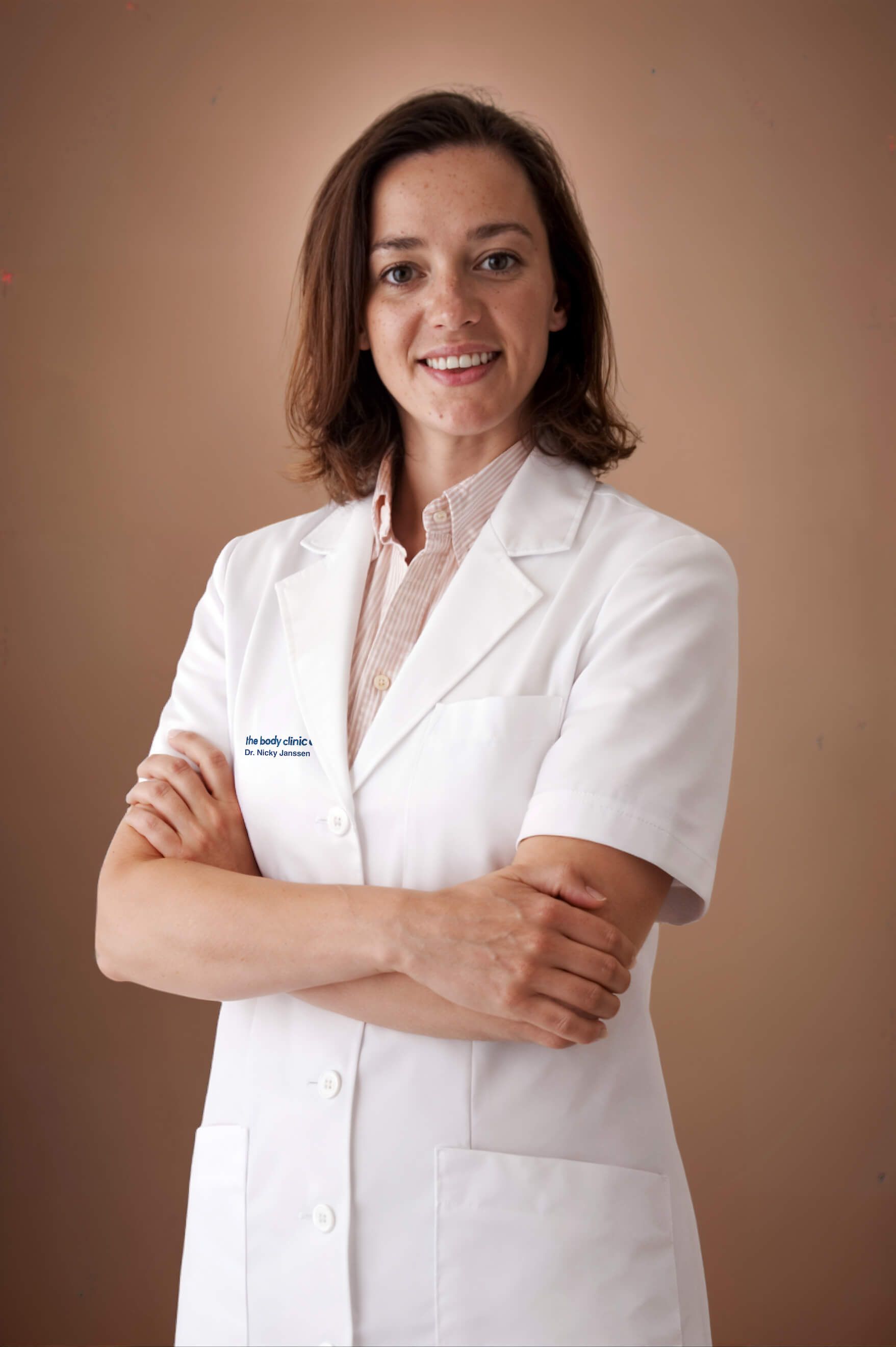 A smiling female medical professional in a white lab coat with crossed arms.