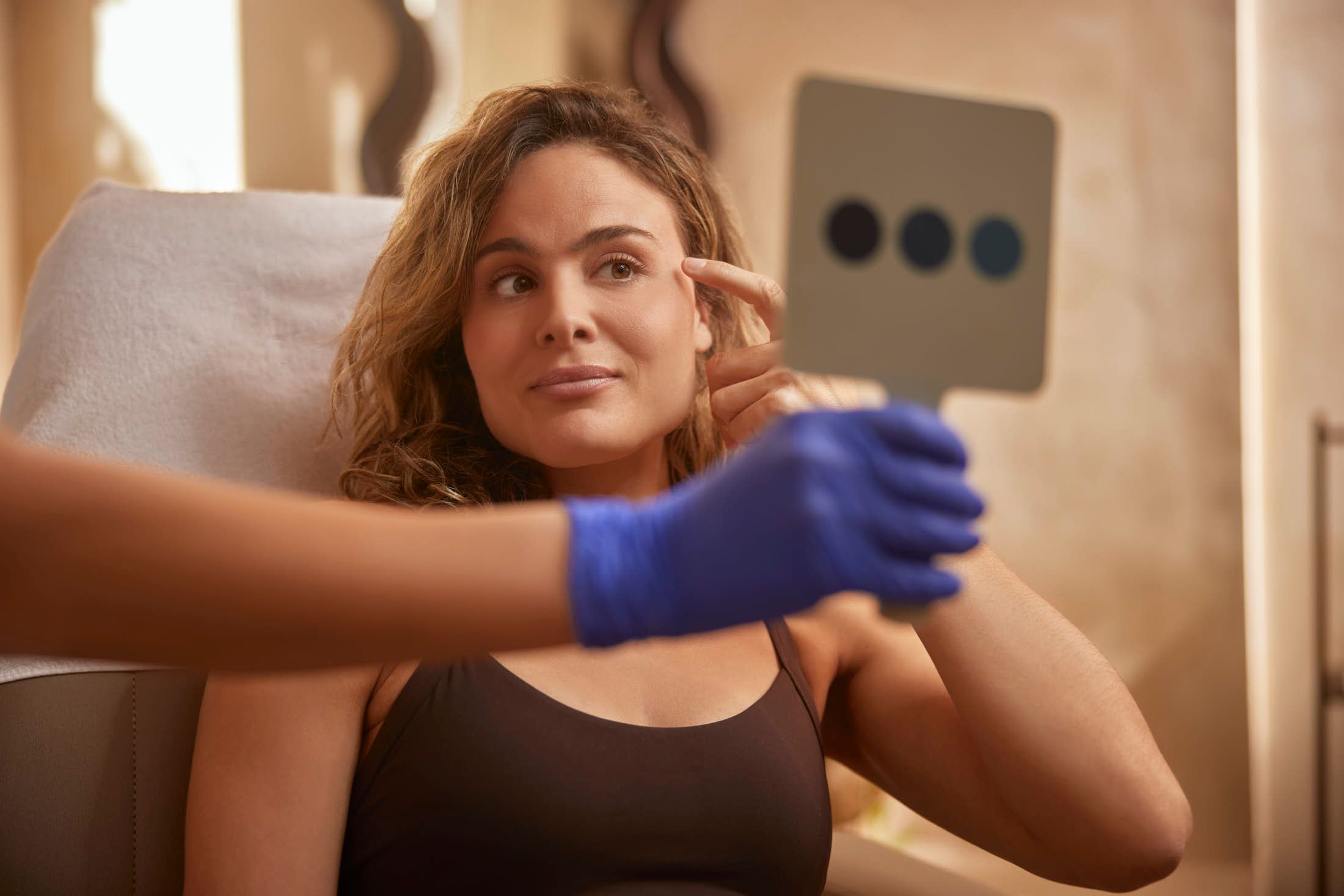 Cliënt bekijkt gezicht in spiegel tijdens botoxconsult bij The Body Clinic