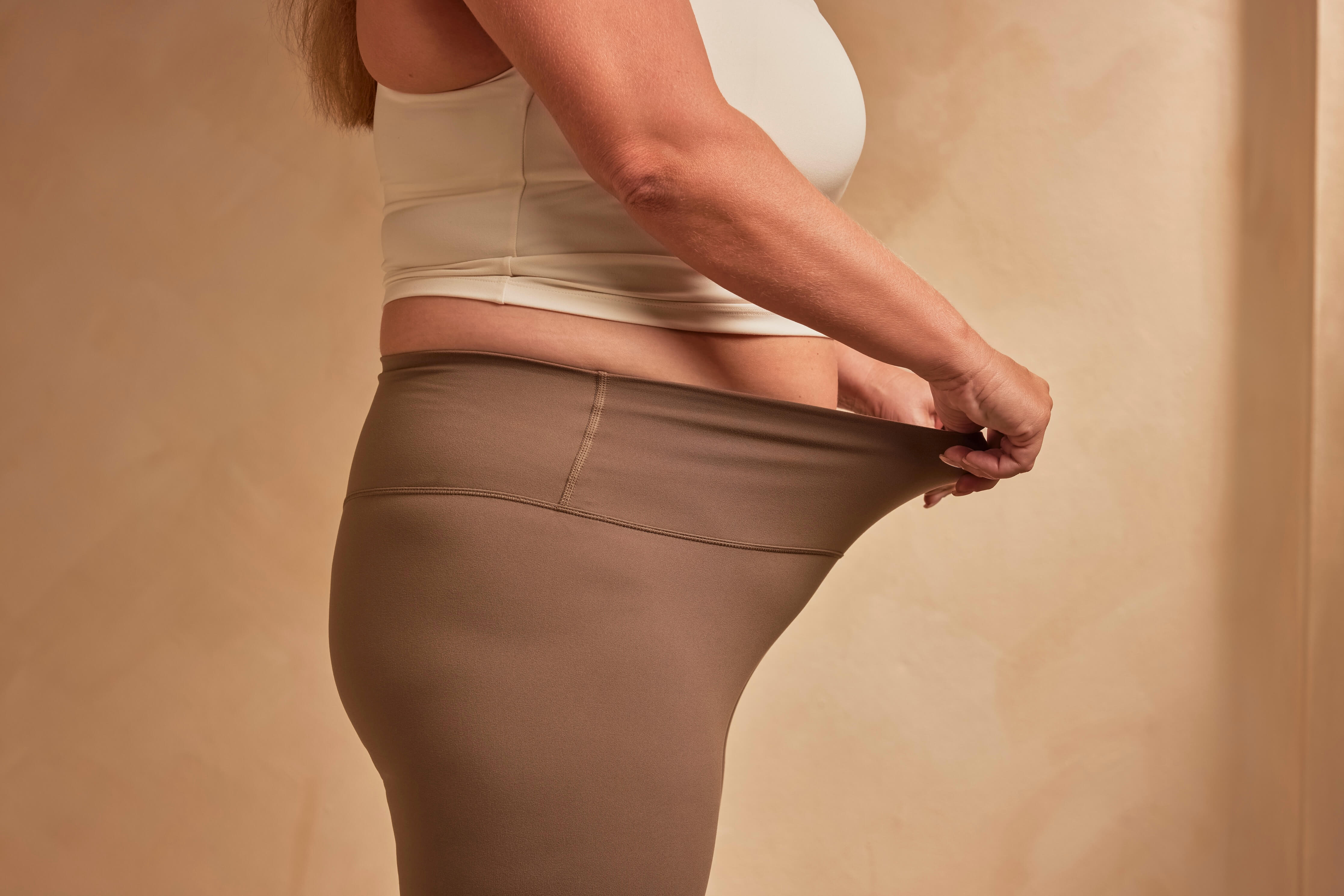 Person in white top pulling up the waistband of brown sheer tights.