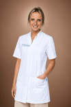Smiling woman in a white medical uniform top with hands in pockets.