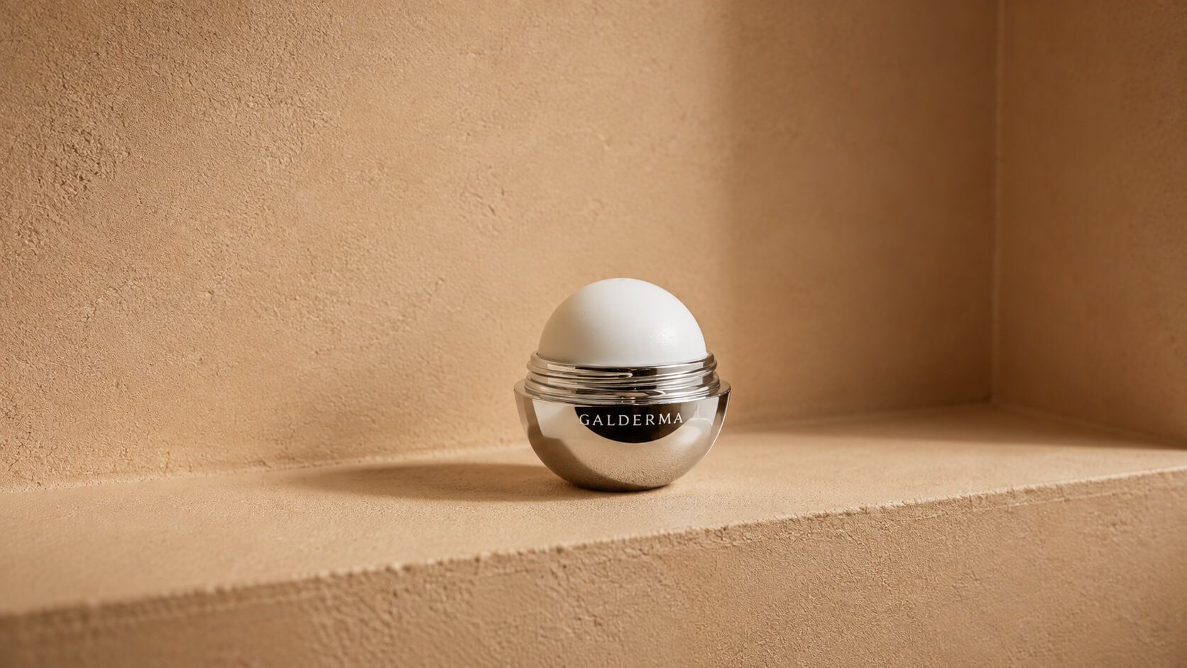 Sleek silver and white egg-shaped cosmetic container by Augustinus Bader on a neutral shelf.