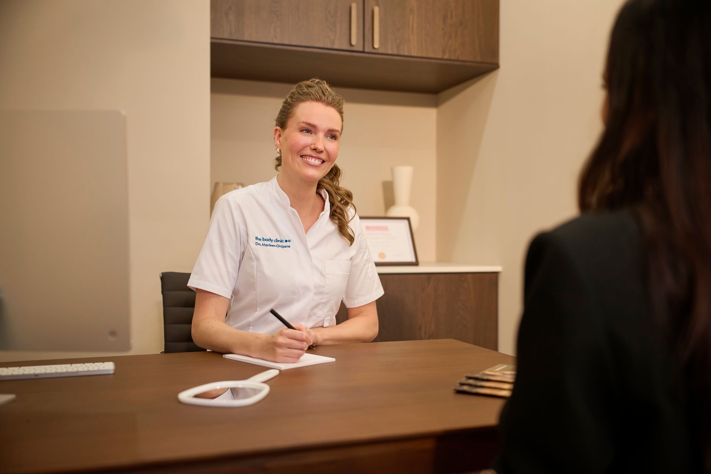 Smiling dental professional consults with a patient at a desk, taking notes.