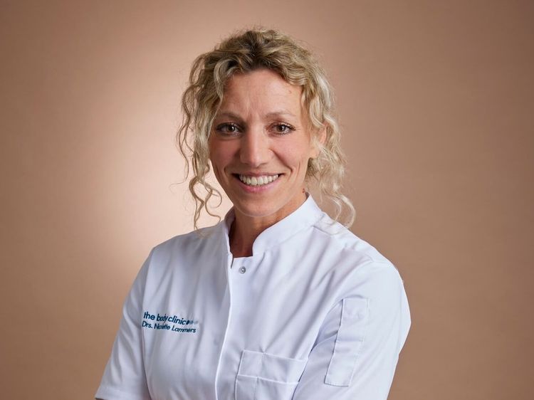 Smiling female doctor with curly blonde hair wearing a white medical coat.
