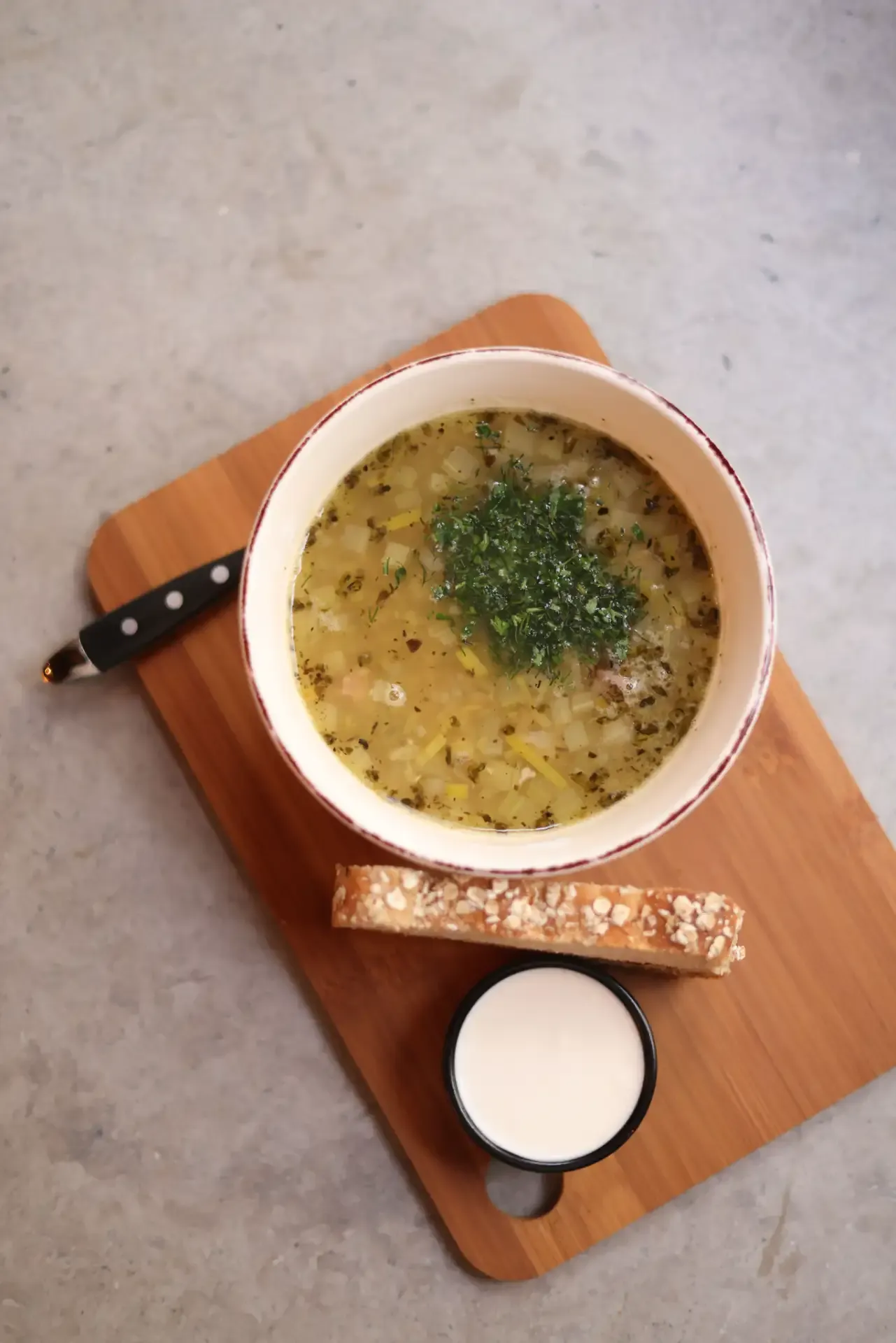 A hearty bowl of vegetable soup with fresh herbs, served with bread and creamy sauce.
