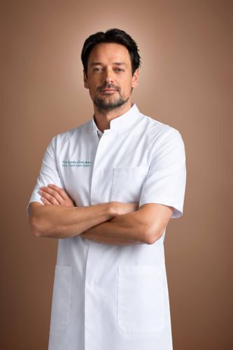 Man in white medical coat with crossed arms and a slight smile.