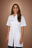 Smiling woman with long dark hair wearing a white medical coat and jeans.