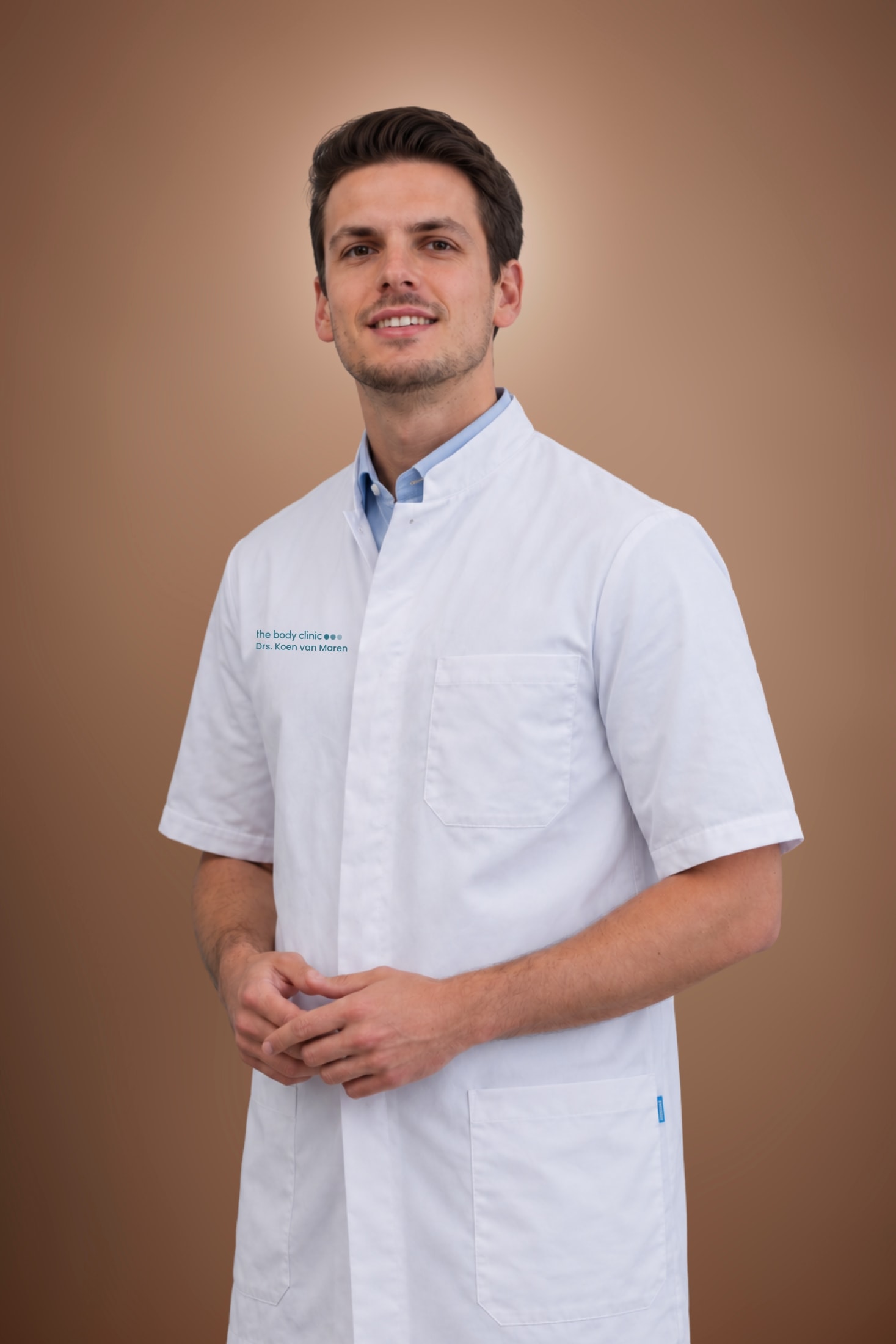 A smiling young man in a white medical coat with a blue collar shirt underneath.
