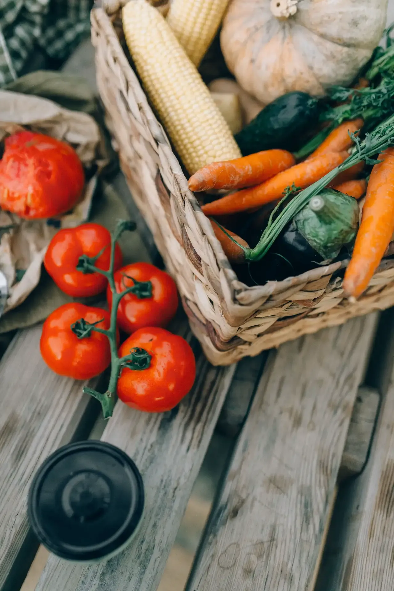 Fresh vegetables, including tomatoes, corn, carrots, and squash, arranged on a rustic wooden table.