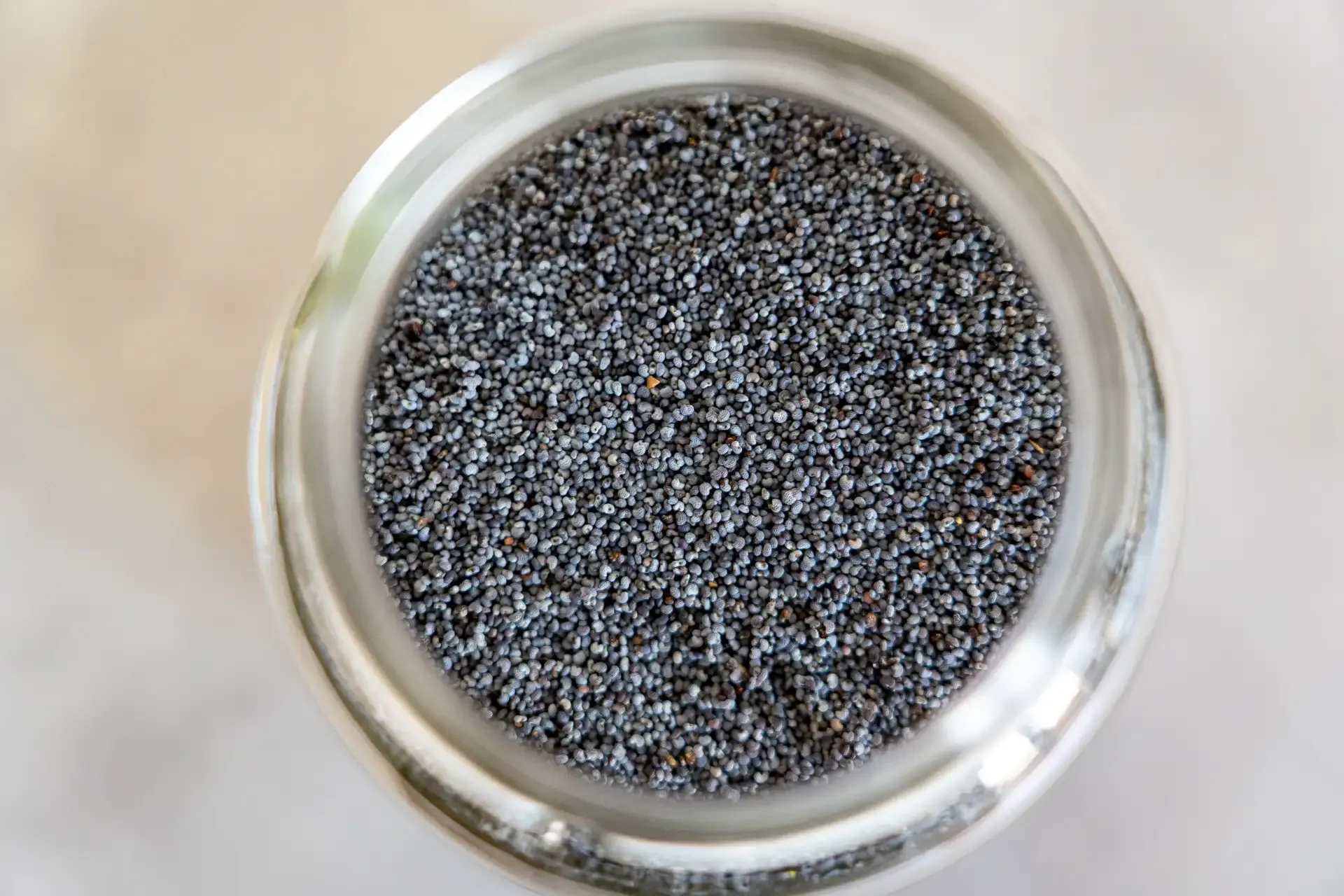 Overhead view of a clear glass jar filled with tiny black poppy seeds.