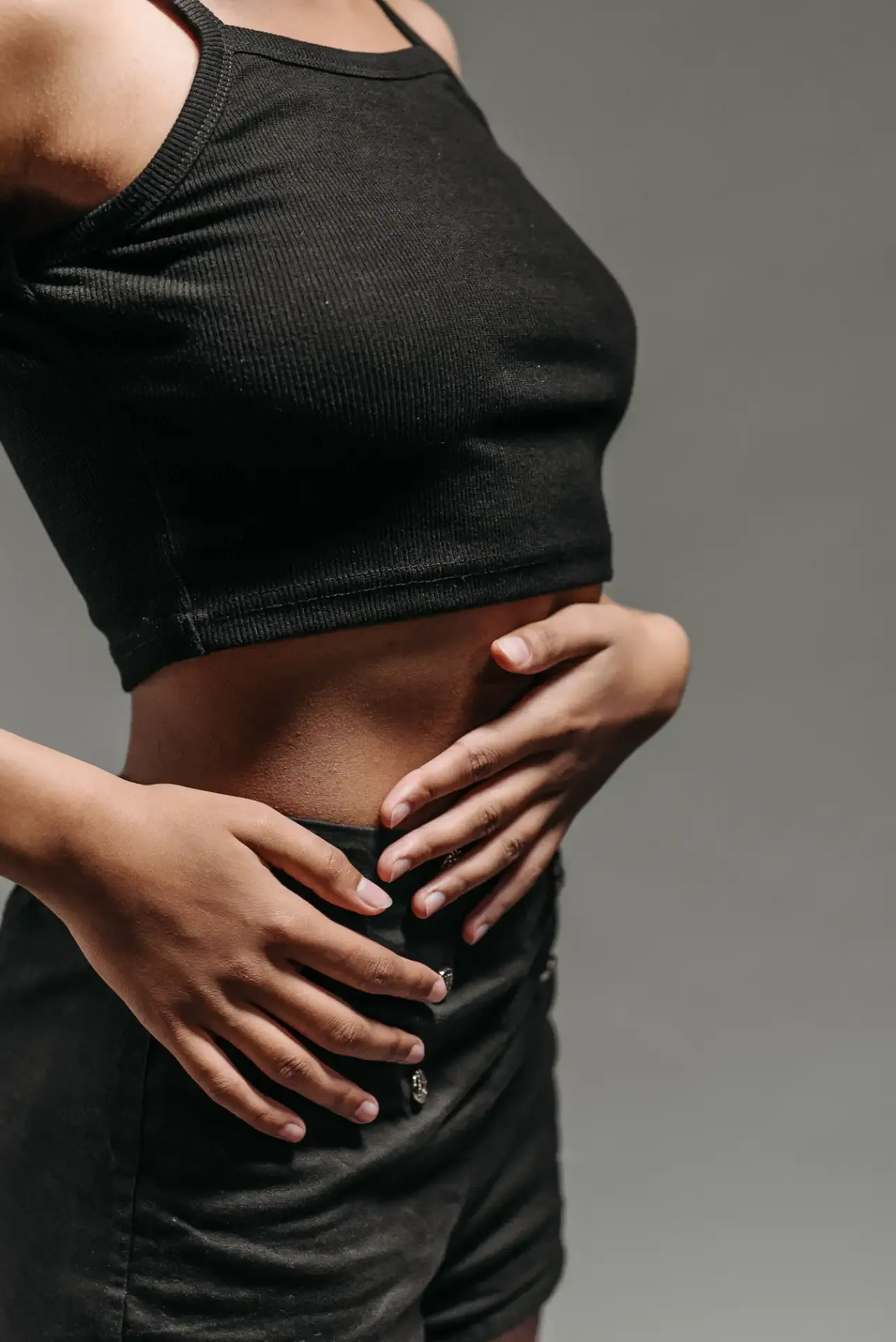 Person's midsection wearing black, with hands gently placed on their stomach.