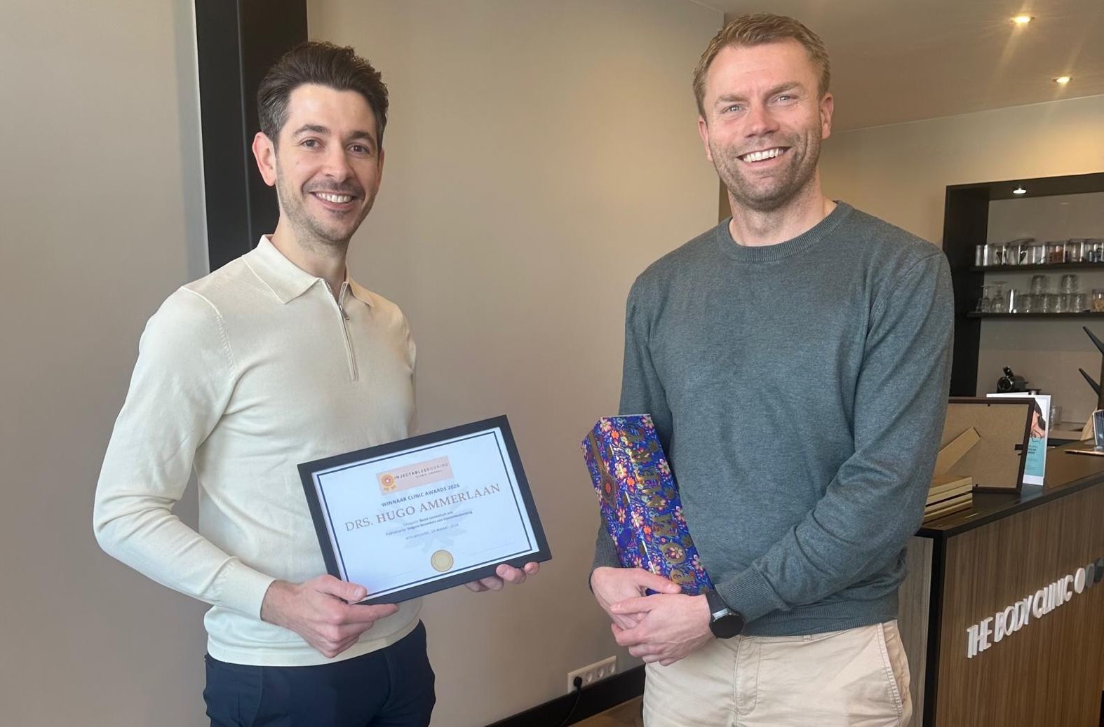 Two smiling men, one holding a framed certificate and the other an award.