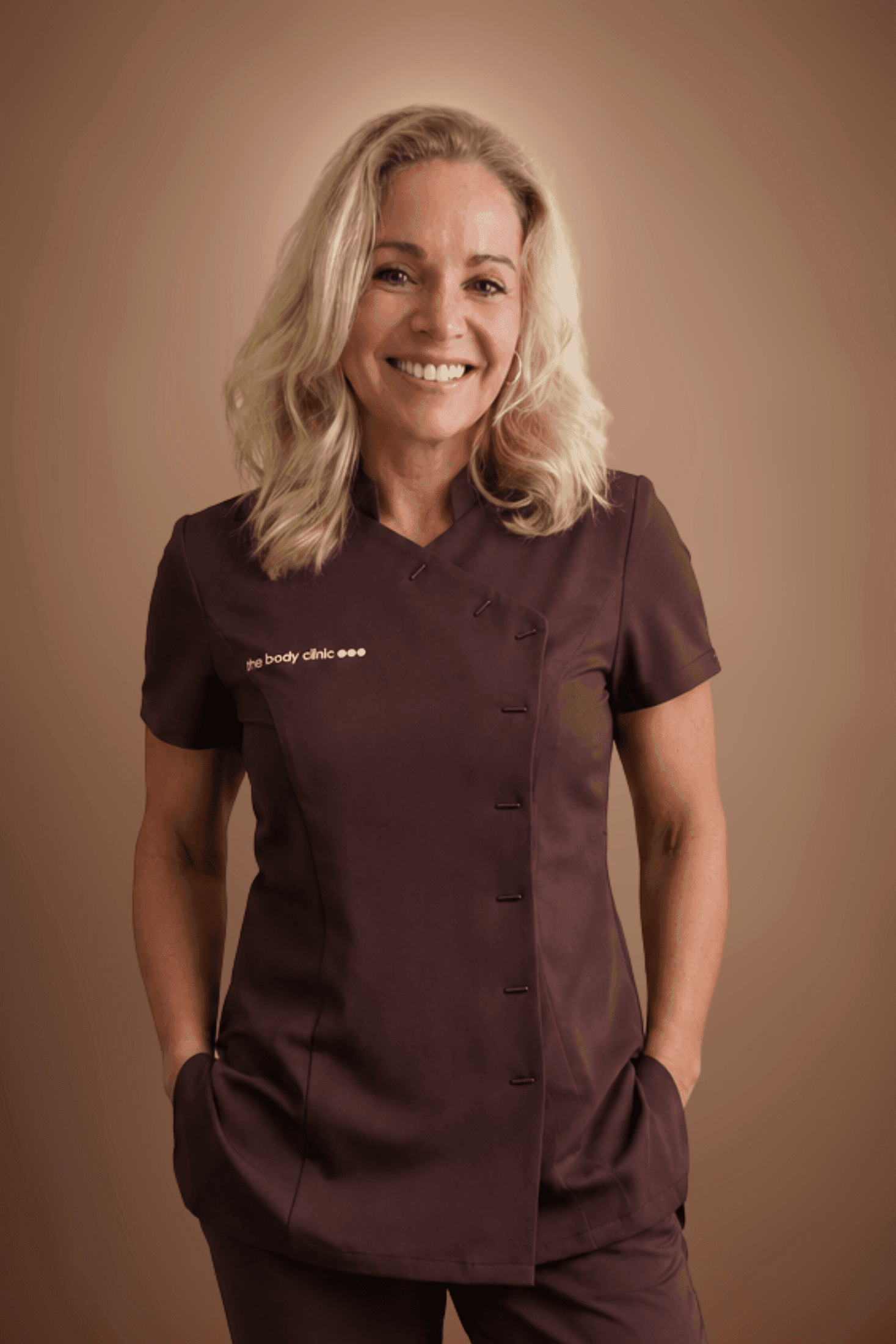 Smiling blonde woman in a brown uniform with hands in her pockets.